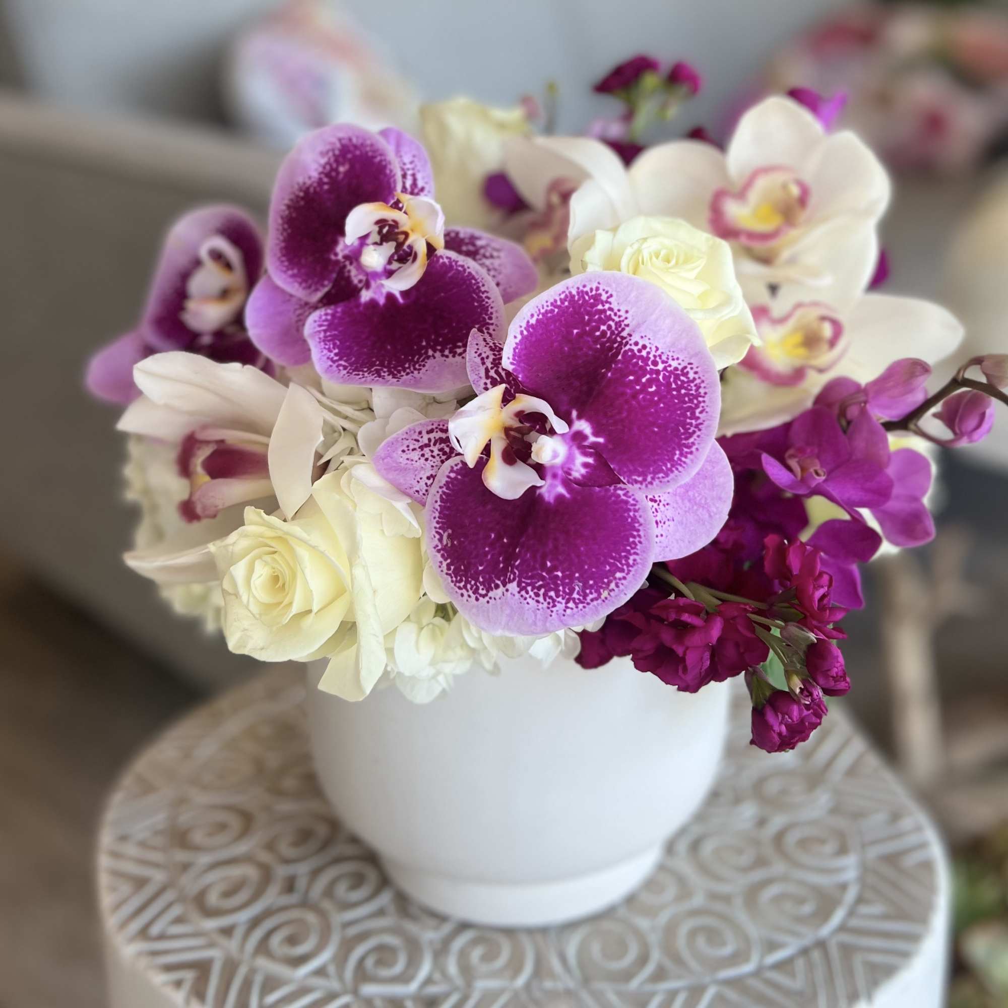Purple and white orchids with cream roses in a white vase