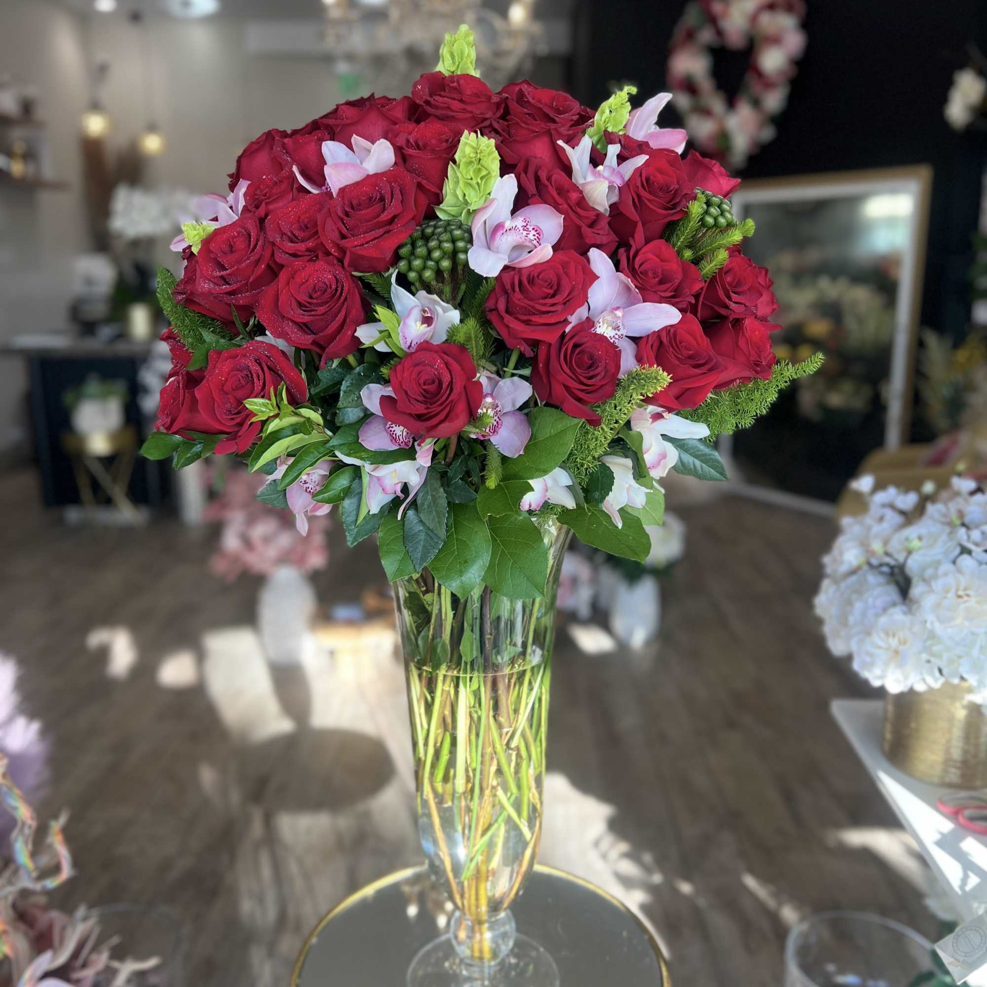 Tall bouquet of red roses and pale pink orchids in a clear glass vase.