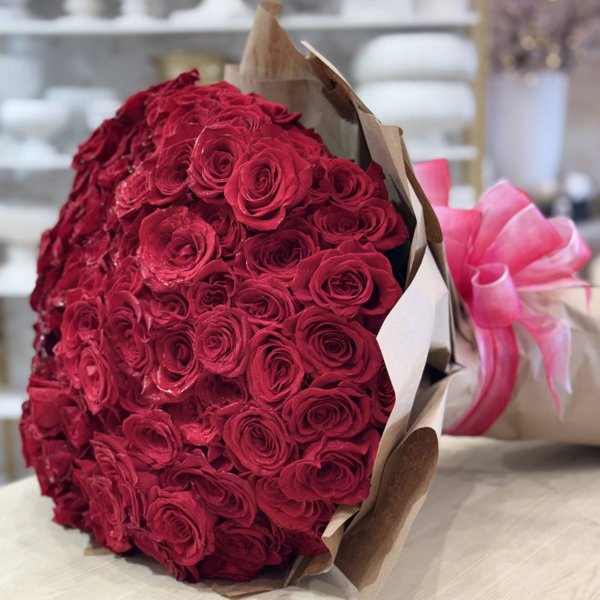 Large bouquet of red roses wrapped in brown paper with a pink ribbon