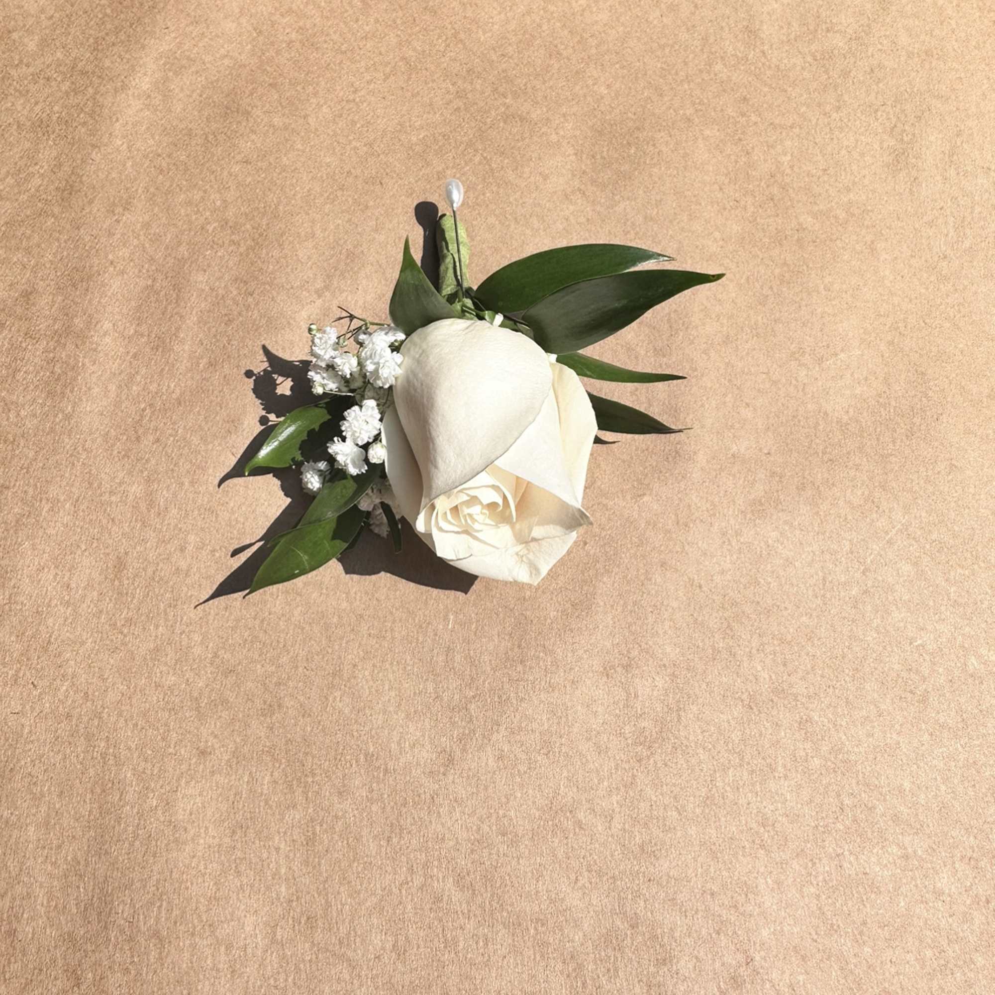 White rose boutonniere with green leaves and baby's breath