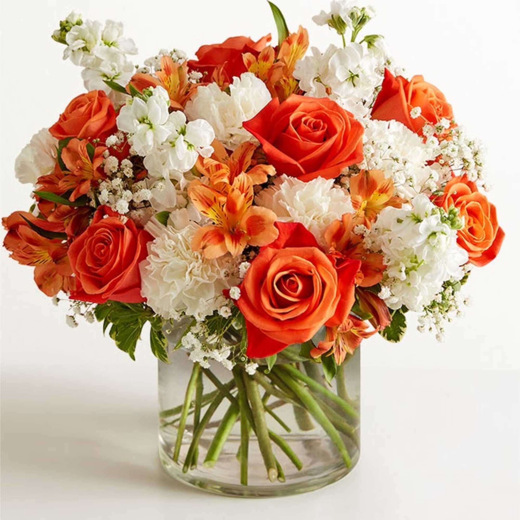 Orange roses and white flowers arranged in a clear glass vase