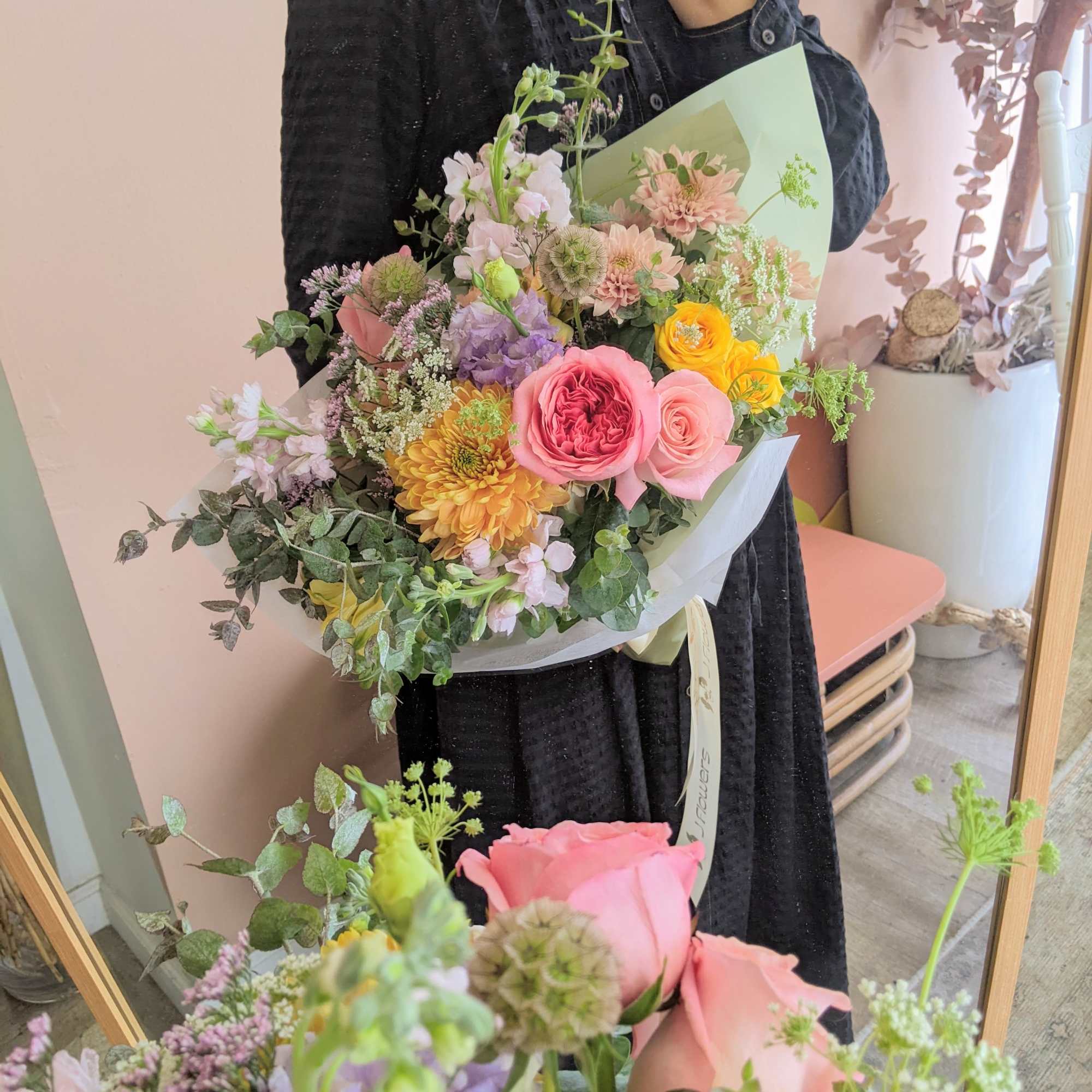 Handheld bouquet of pink, yellow, and lavender flowers wrapped in pale paper