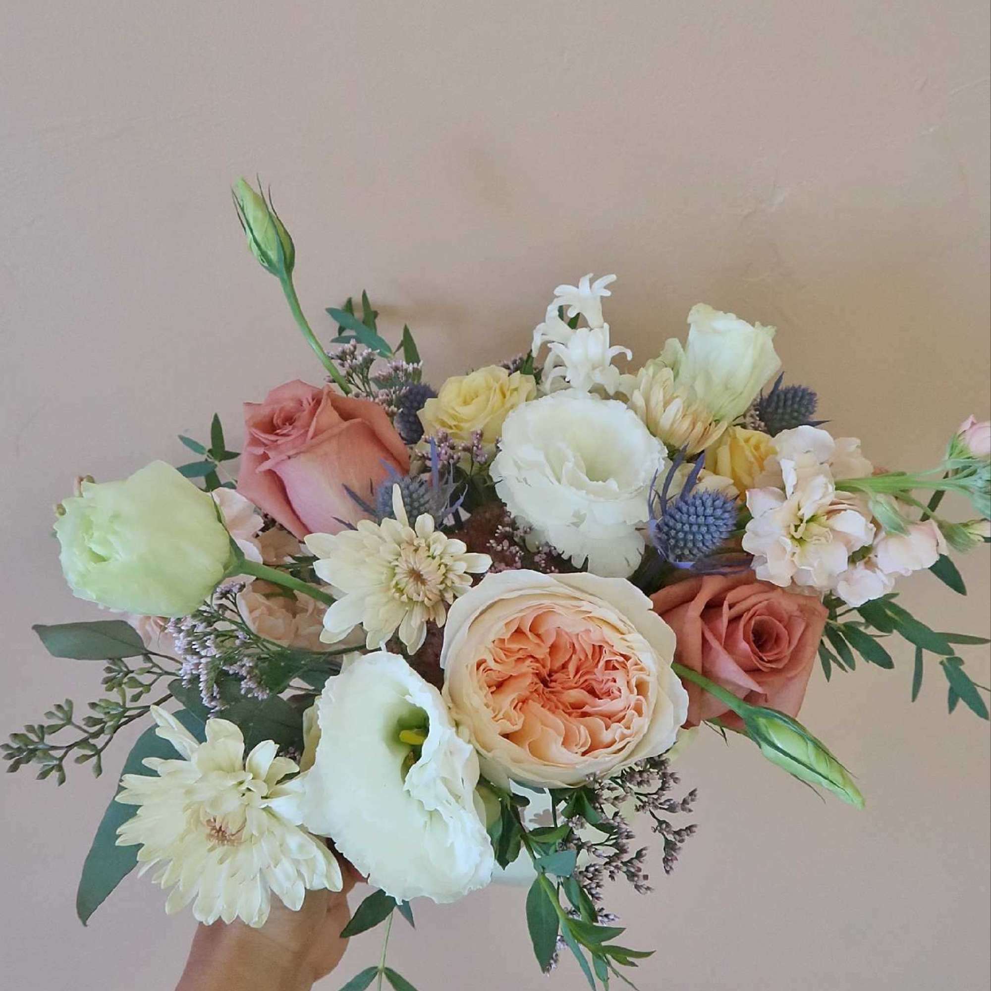Handheld bouquet of peach and white roses with pale blooms and greenery