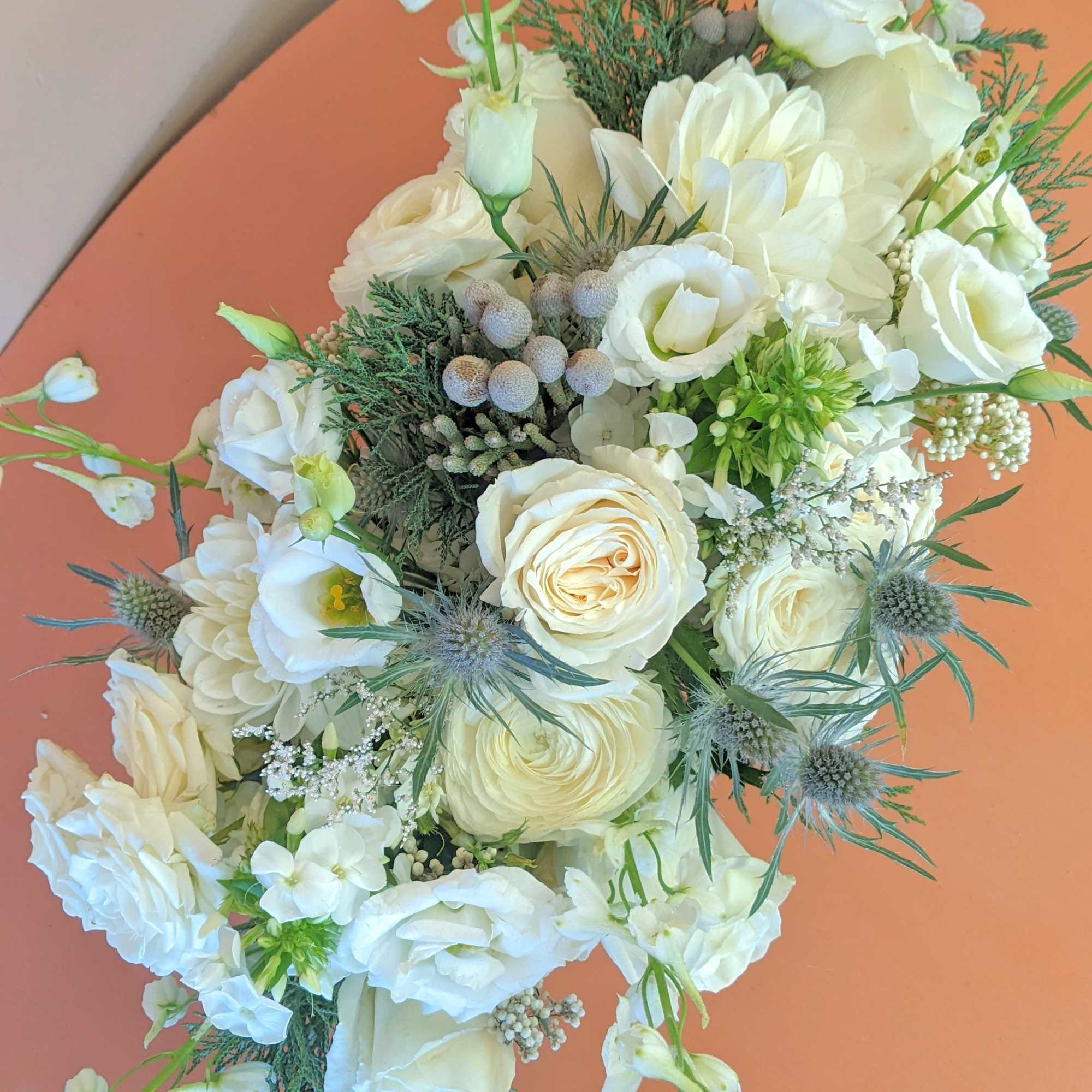 White floral bouquet with roses and lisianthus on an orange table