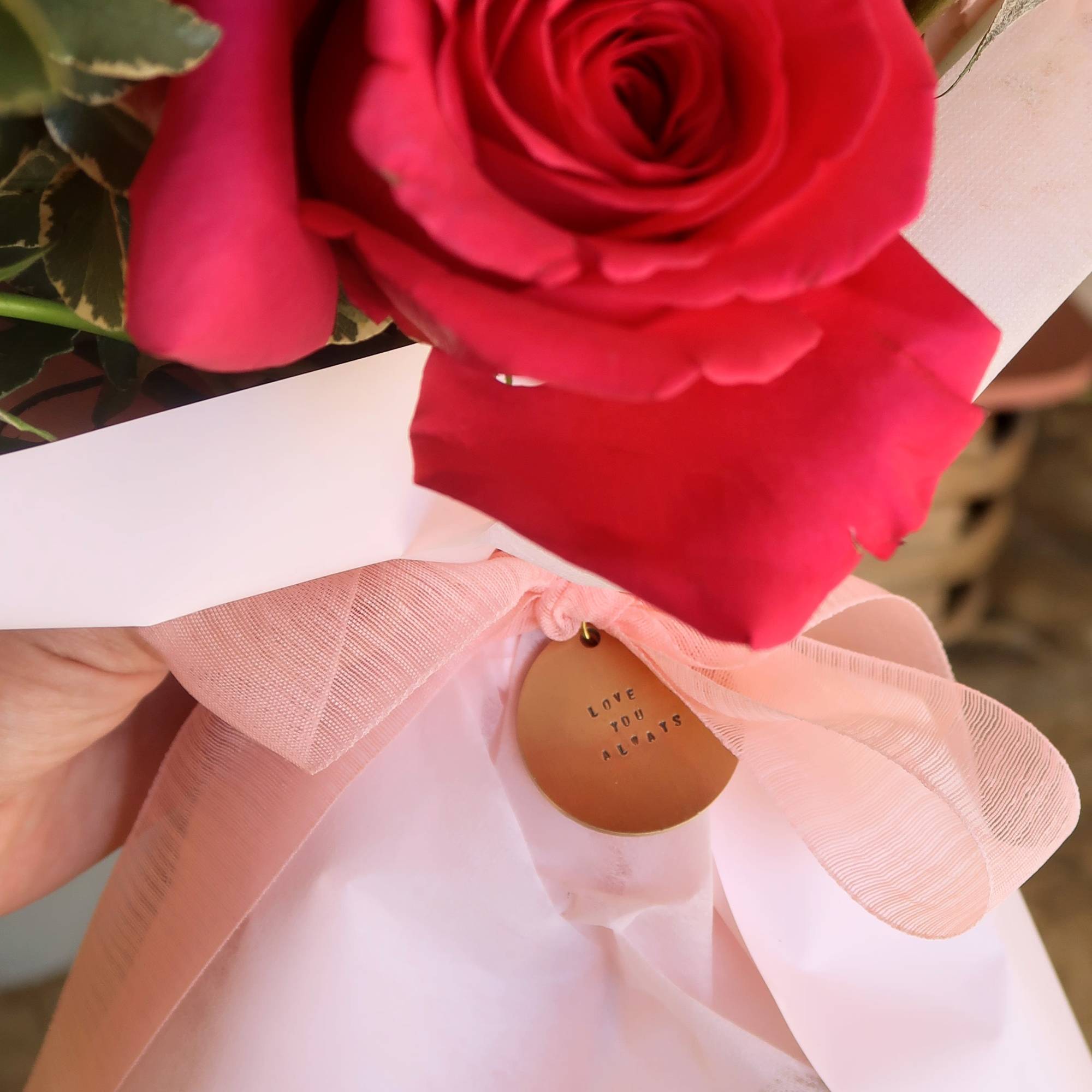 Close-up bouquet of red roses wrapped with a pink ribbon and tag