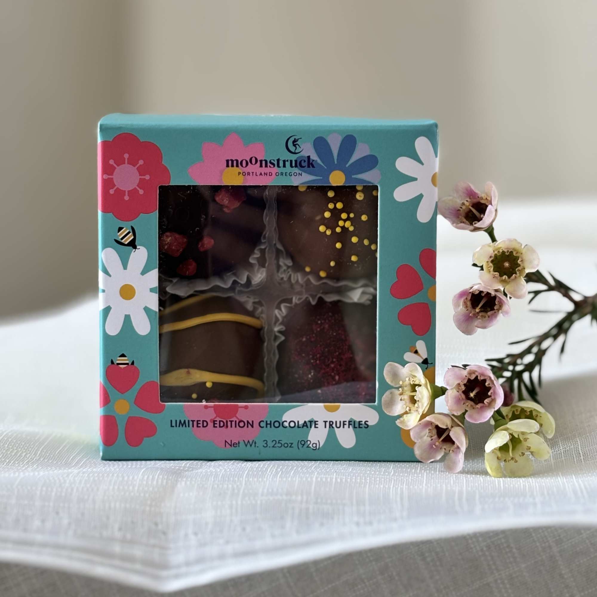 Box of chocolate truffles beside a small sprig of pink and white flowers
