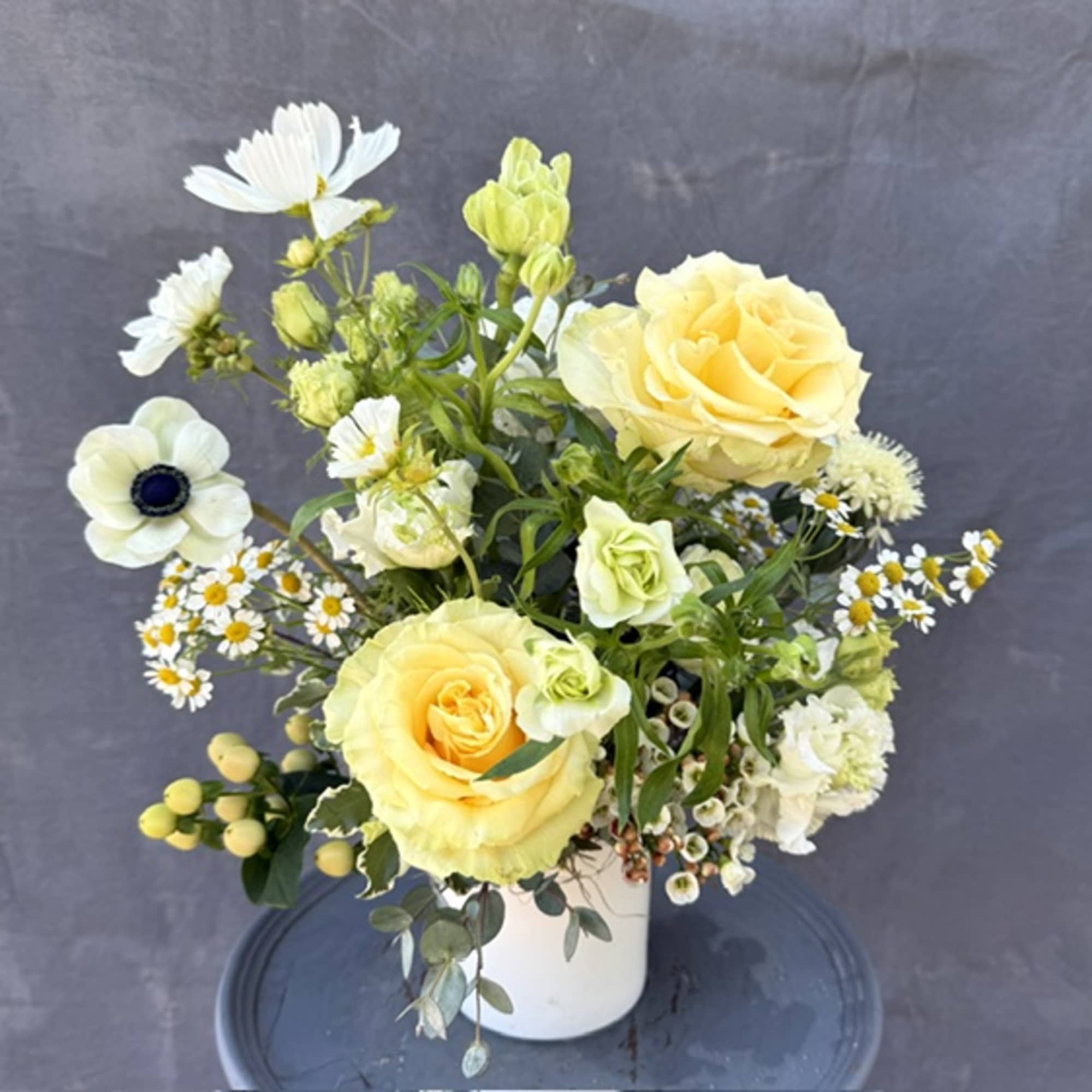 Yellow roses and white flowers arranged in a white vase