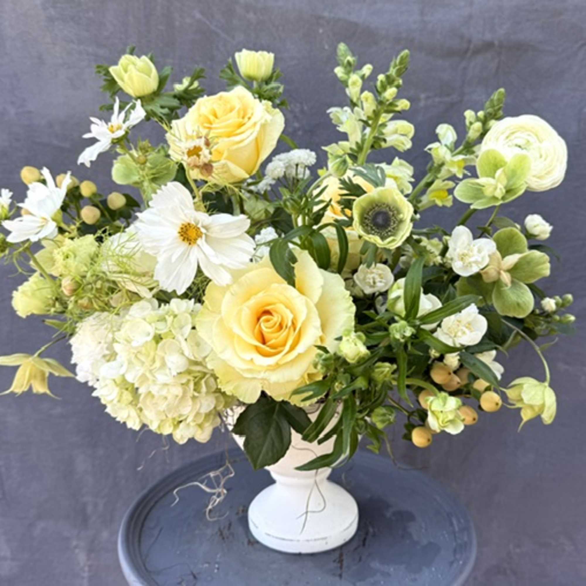 Yellow roses and white flowers arranged in a white vase