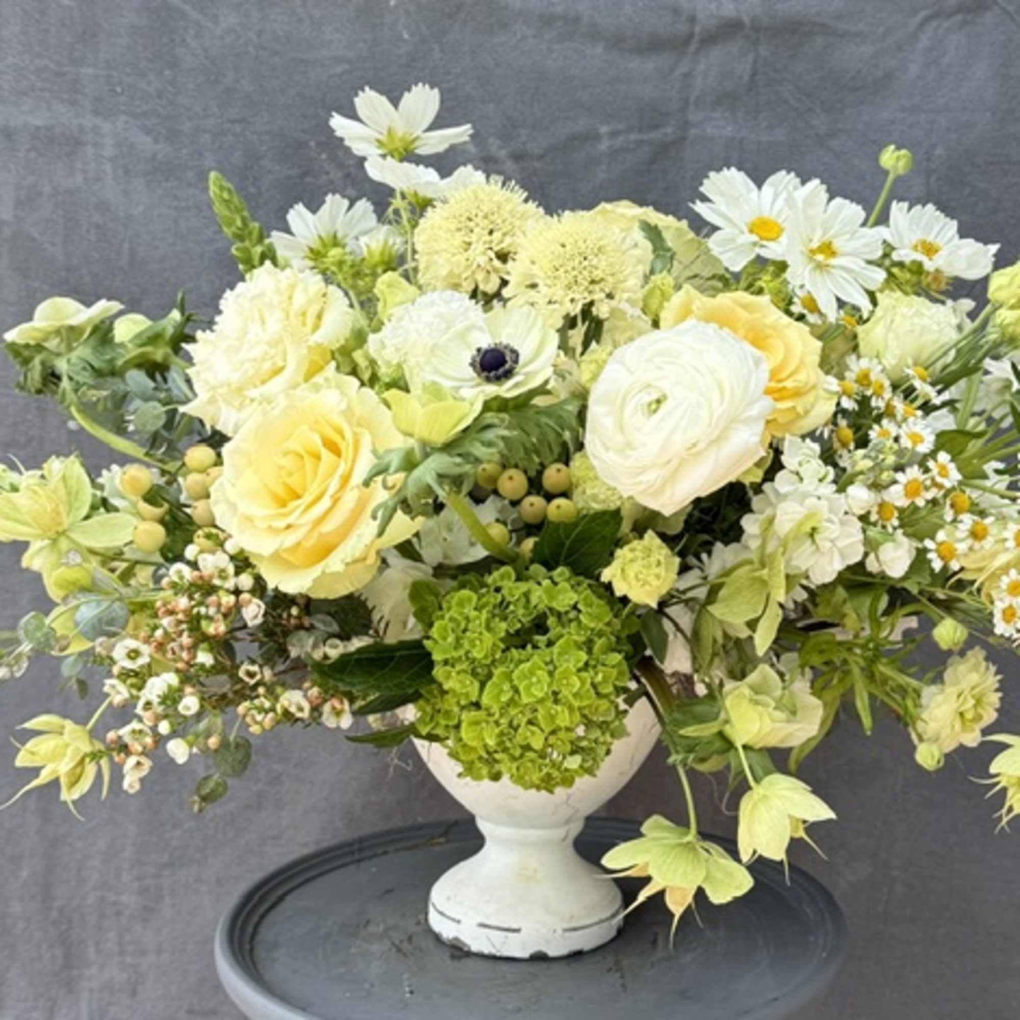 Yellow and white mixed flower arrangement in a white pedestal vase