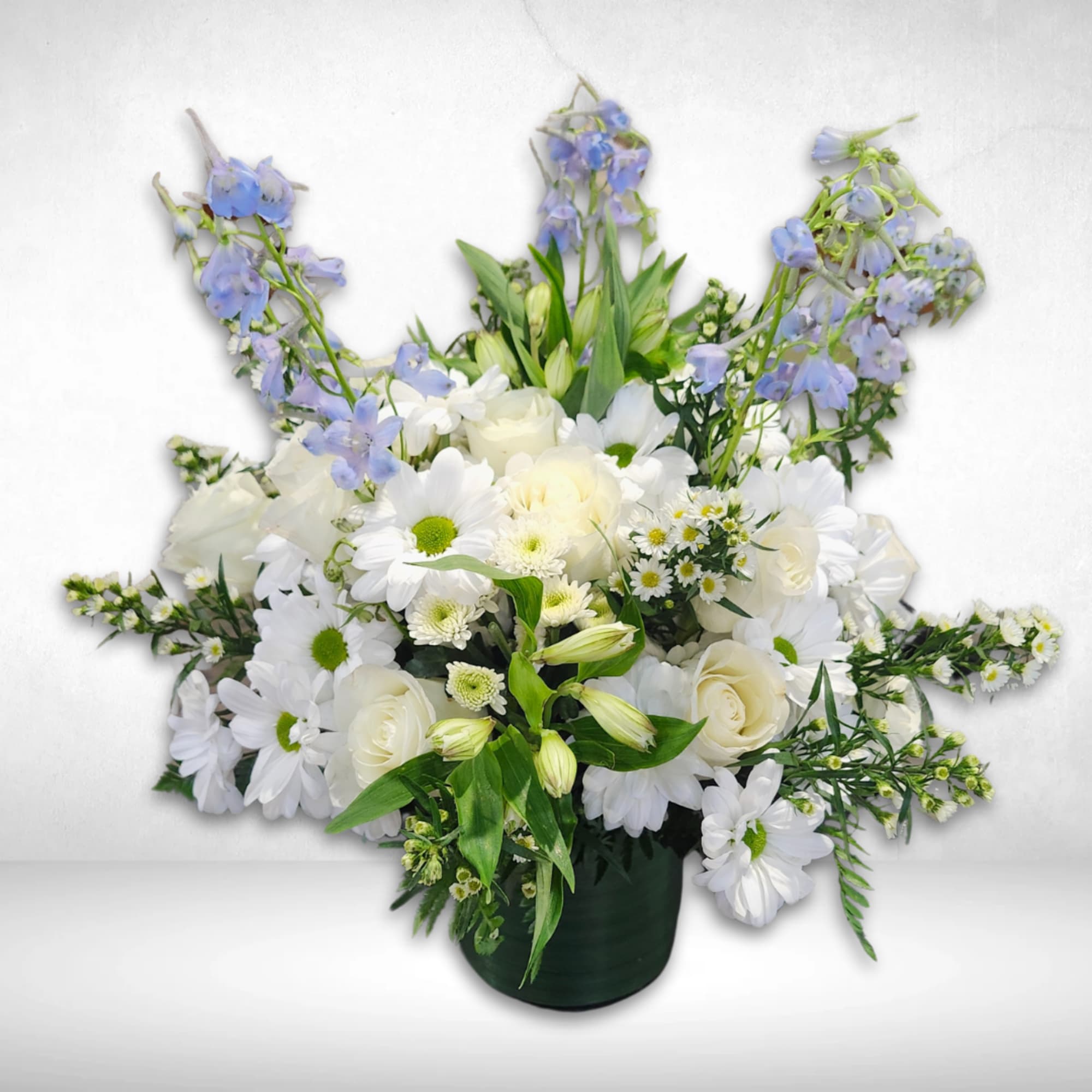 White daisies and roses with blue delphinium in a dark vase