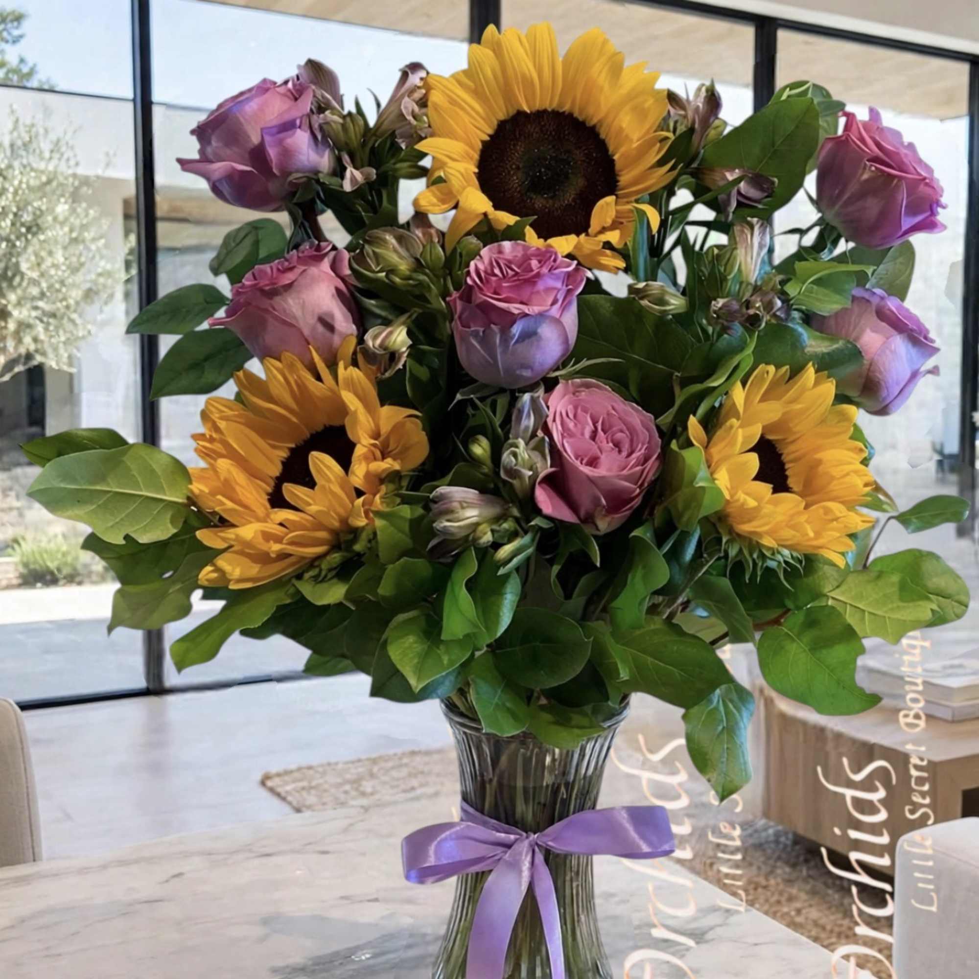 Bouquet of sunflowers and pink roses in a glass vase with a purple ribbon