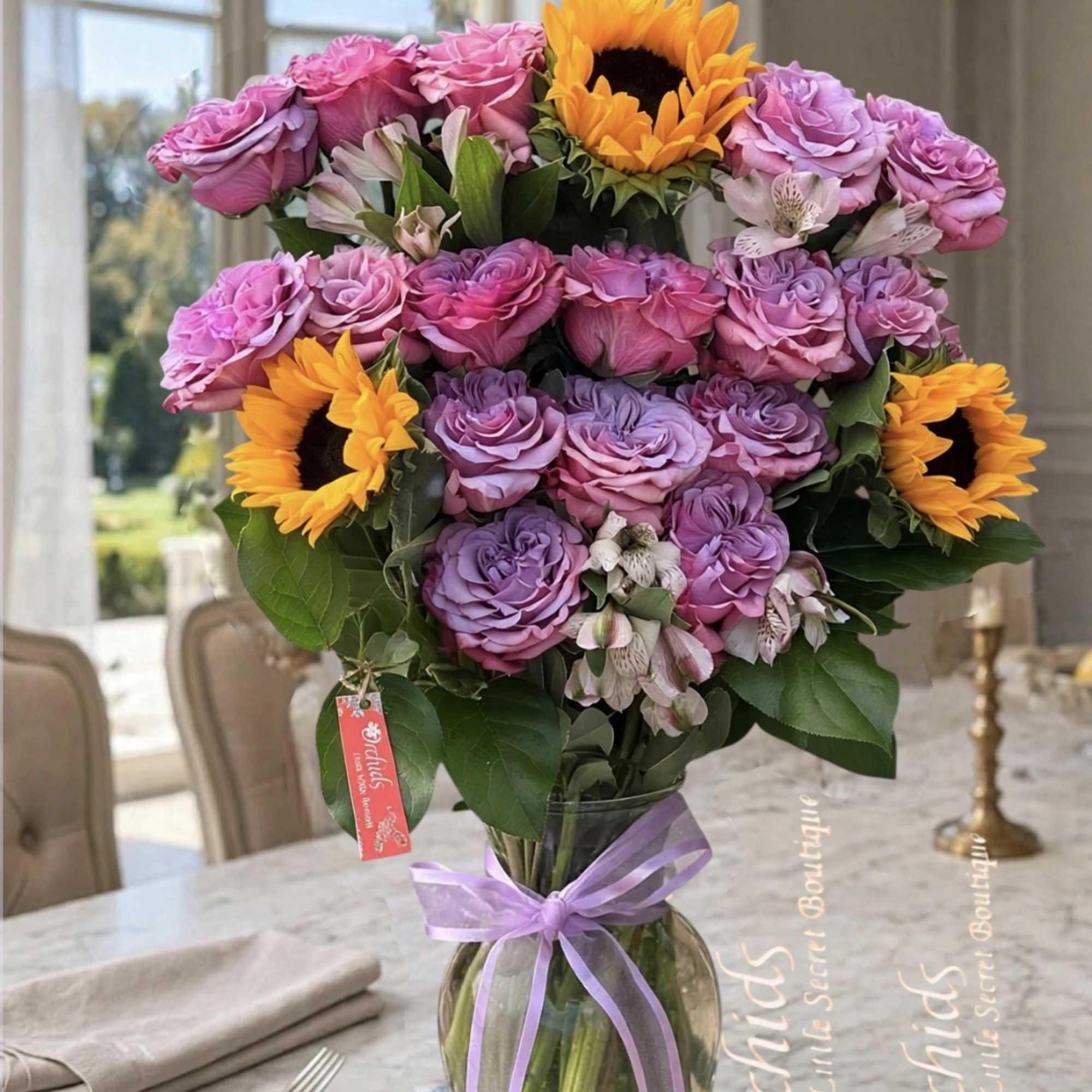 Bouquet of pink and lavender roses with sunflowers in a glass vase