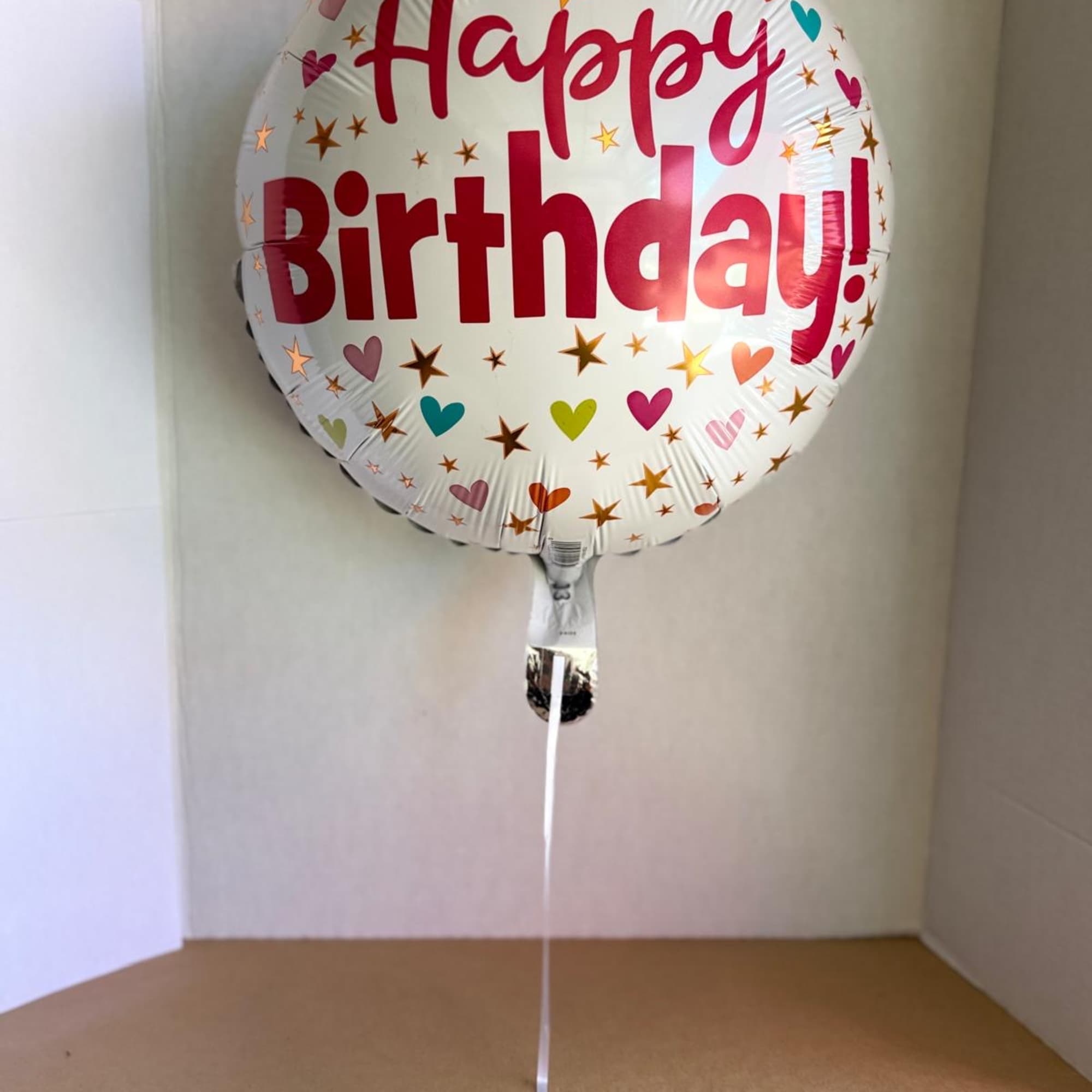 Round foil balloon reading Happy Birthday with heart and star confetti