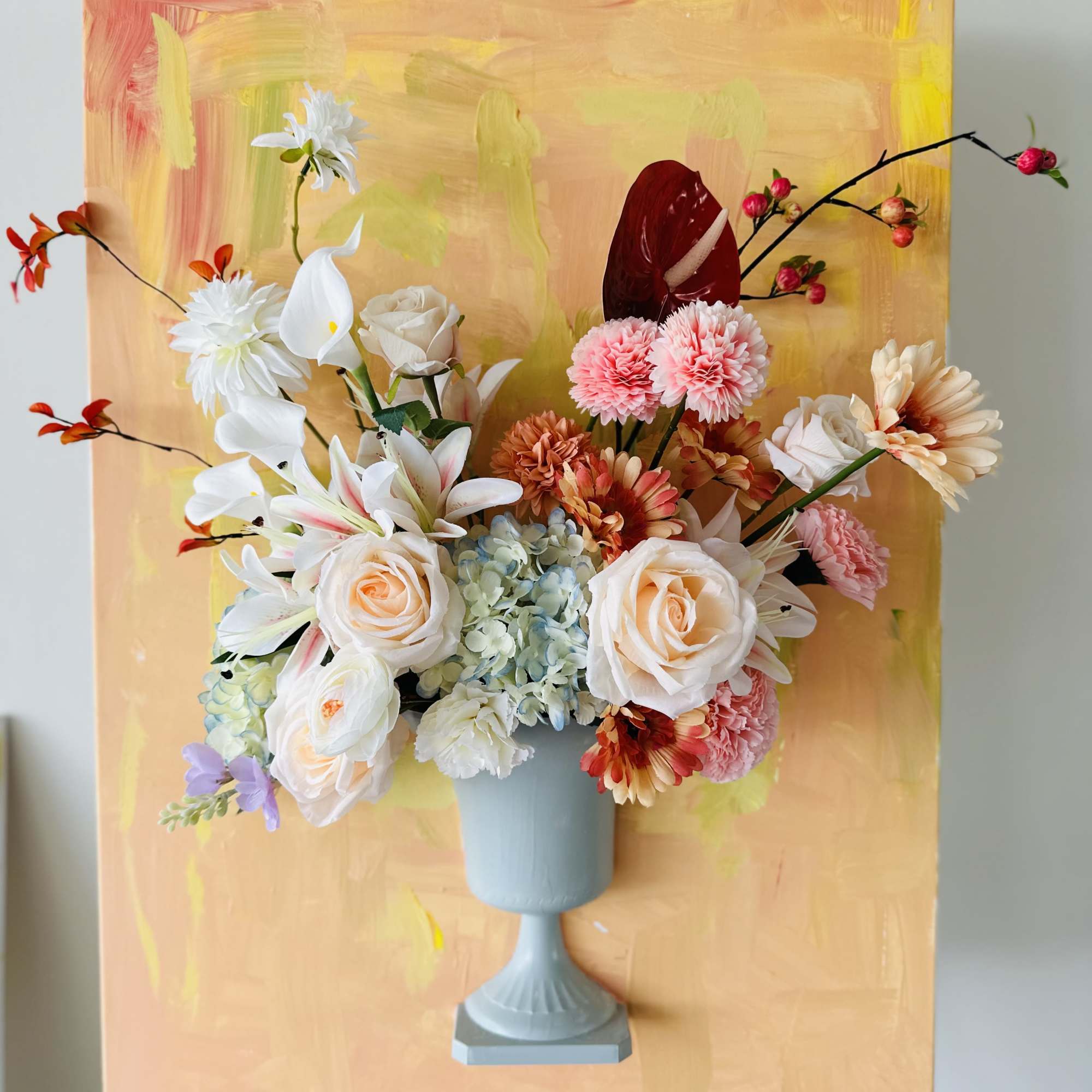 Mixed floral arrangement in a blue pedestal vase against a painted backdrop, photo 2 of 2