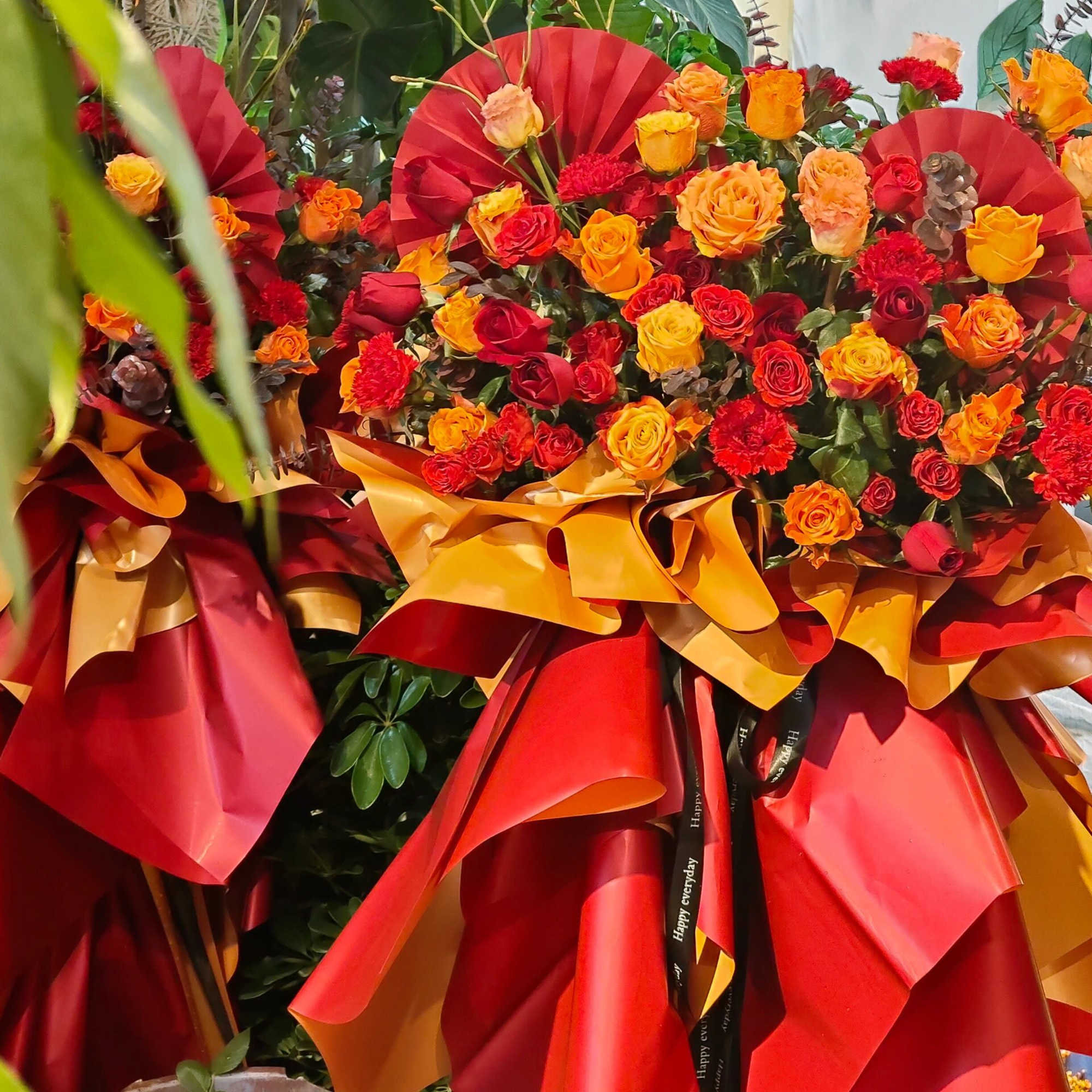 Large bouquet of red, orange, and yellow roses wrapped in red and gold paper