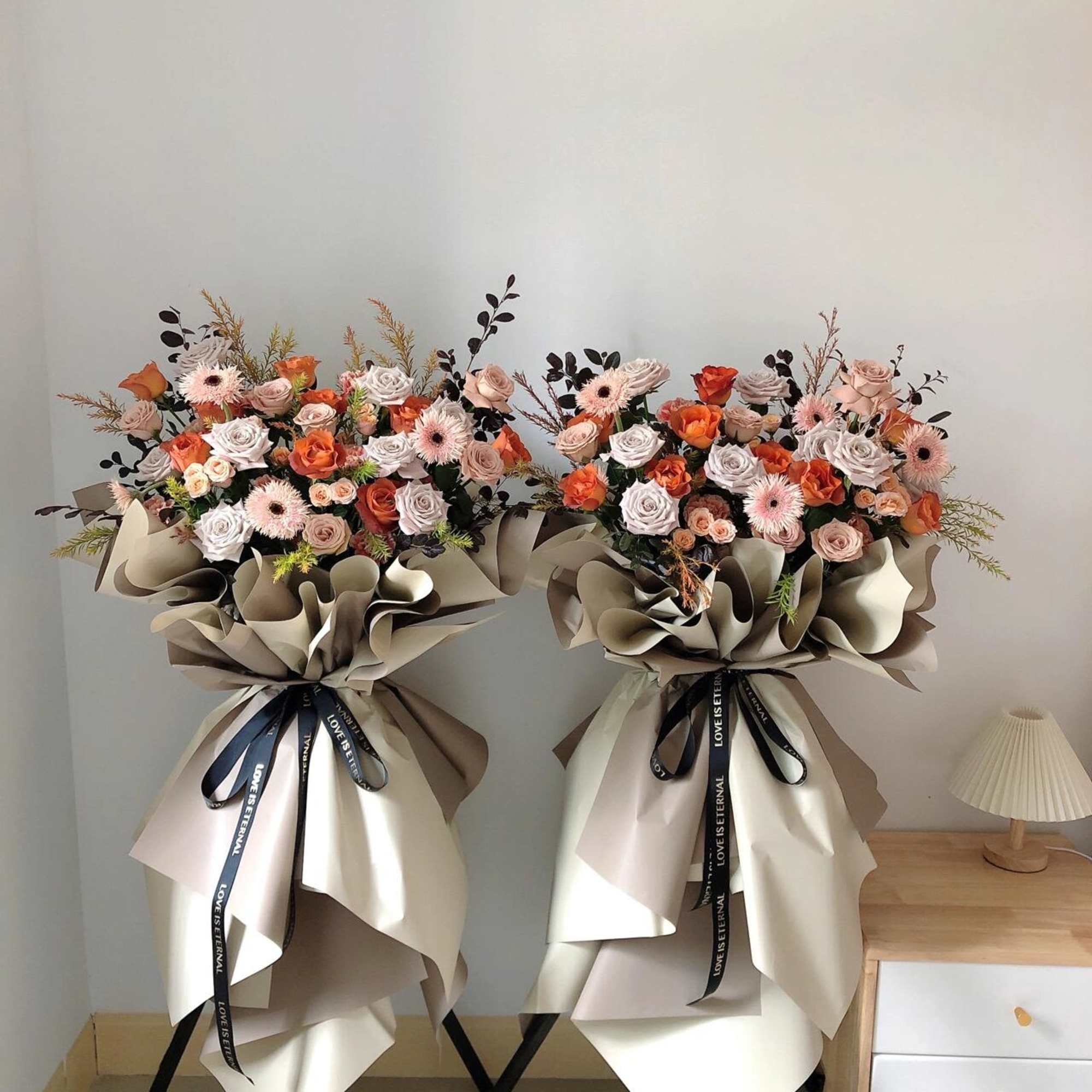 Two large bouquets of roses and gerbera daisies wrapped in beige paper