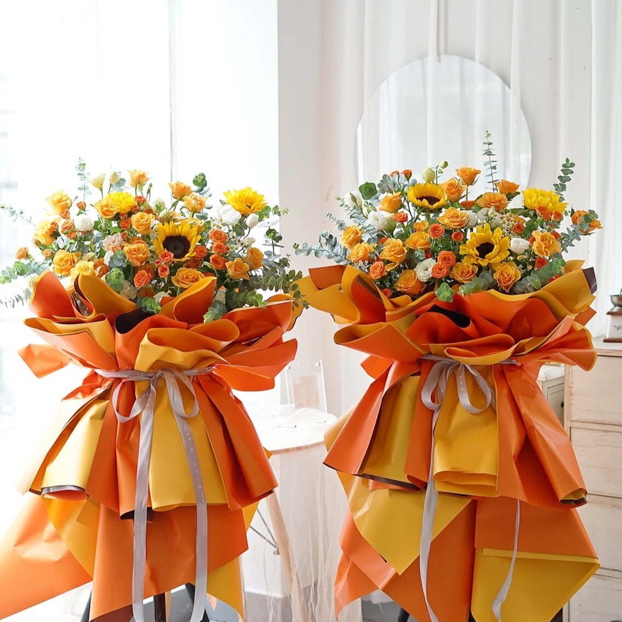 Two orange and yellow bouquets with sunflowers and roses