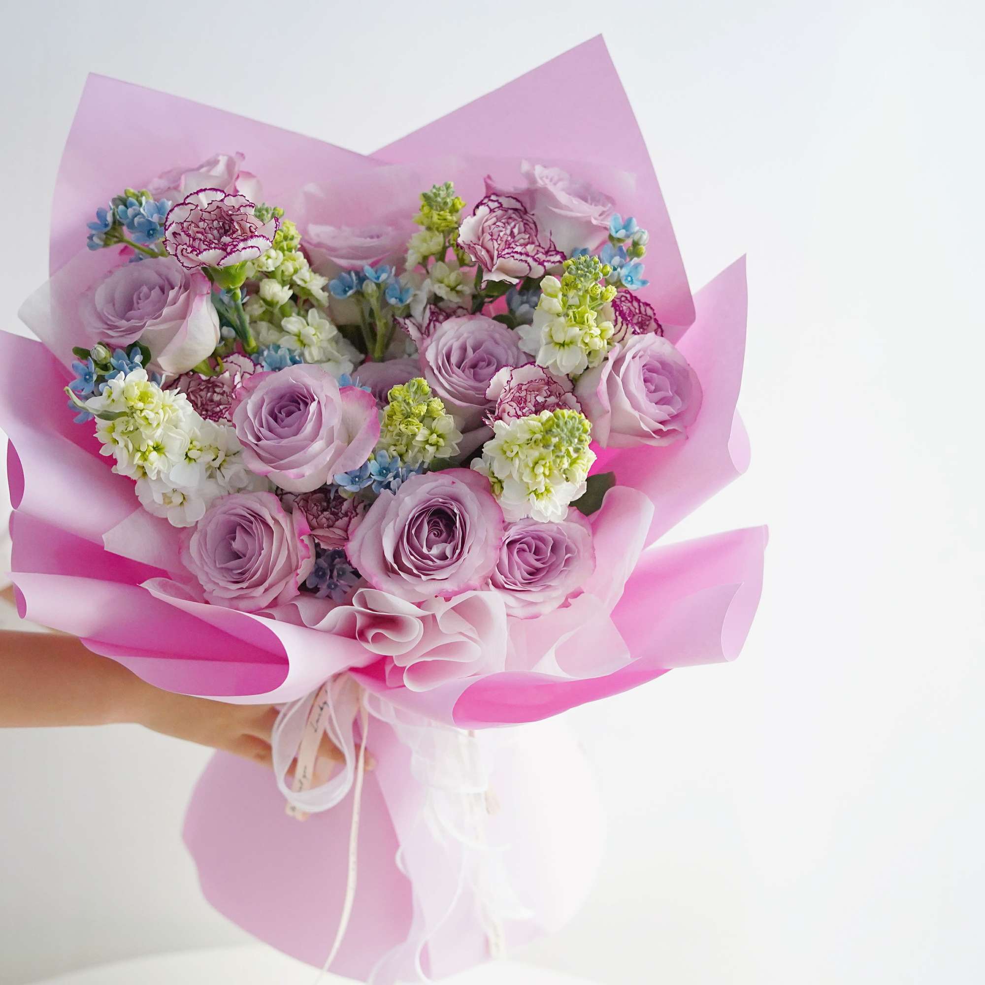 Pink bouquet of roses, carnations, and small blue flowers wrapped in pink paper