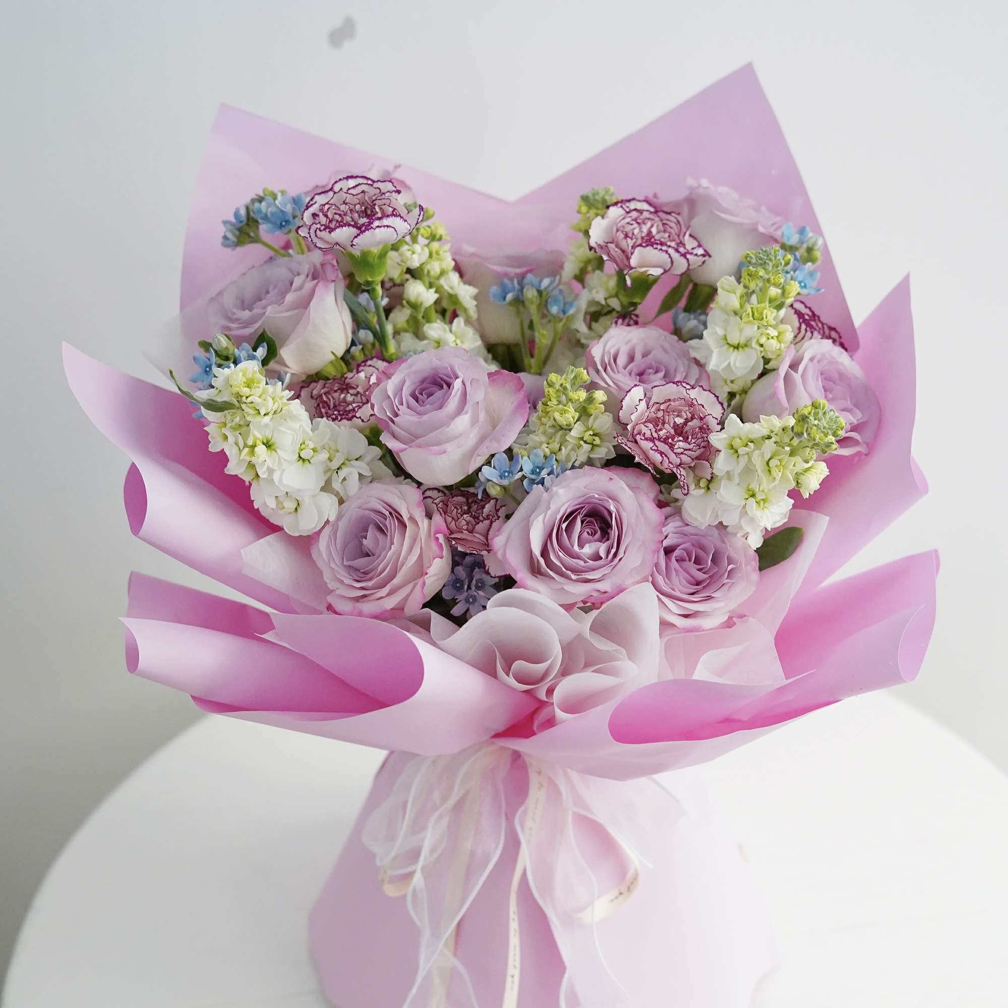 Bouquet of lavender roses and pink-edged carnations wrapped in pink paper
