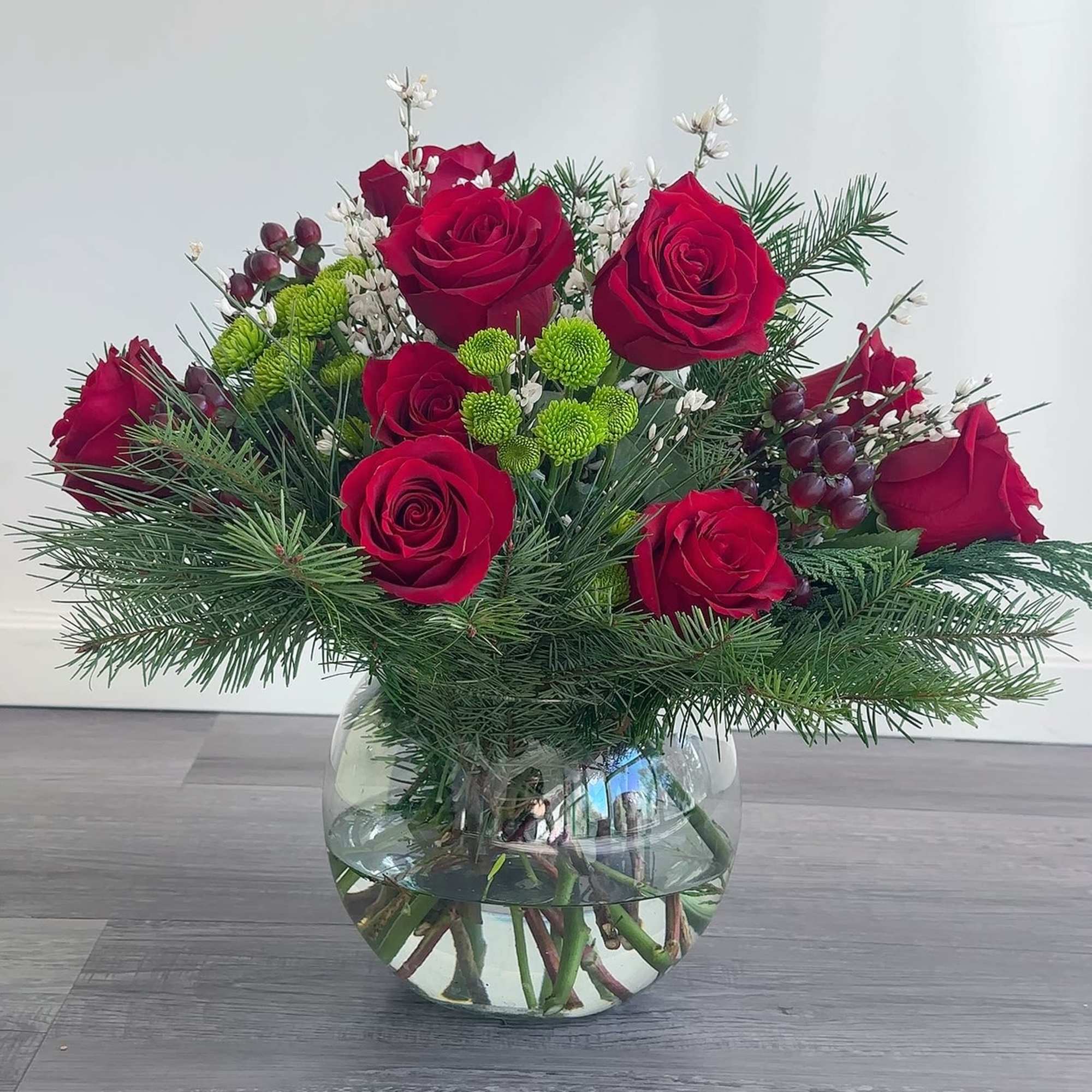 Red roses in a glass vase with pine and small white accents