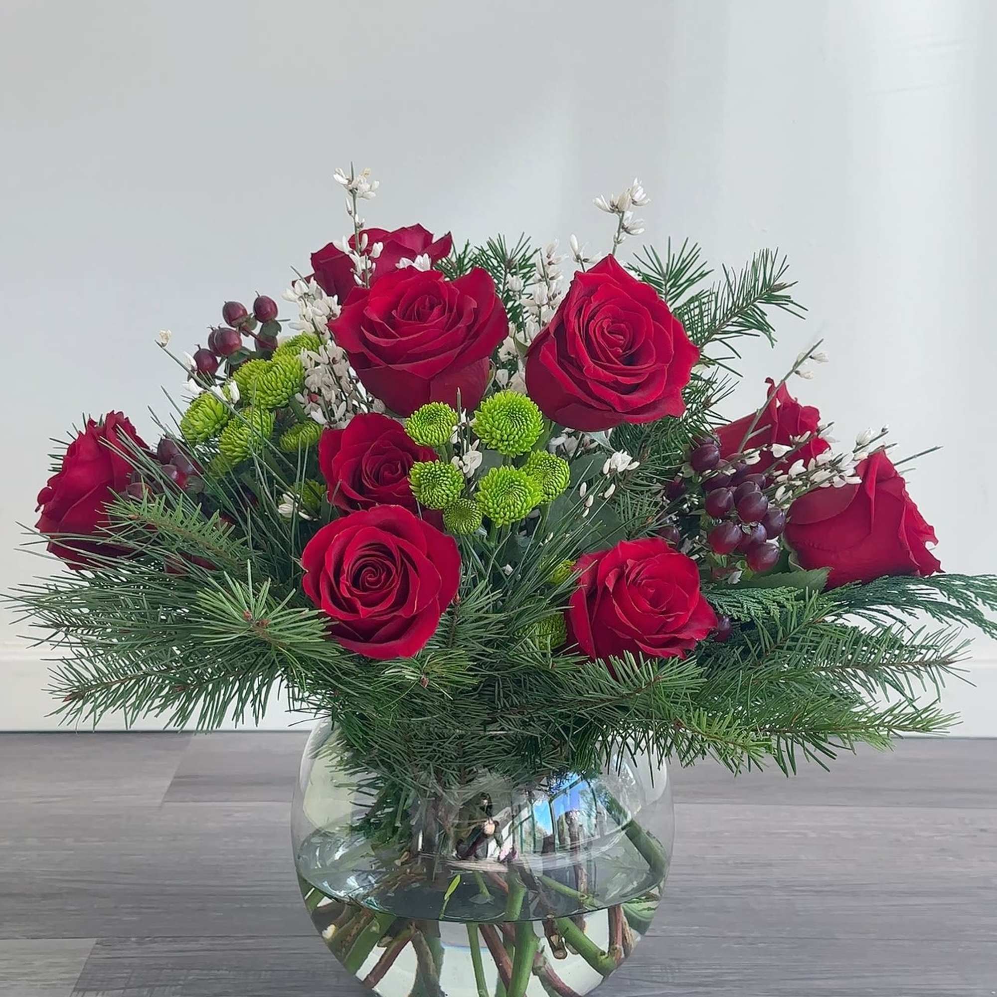 Red roses arranged in a clear glass vase with pine and small green accents