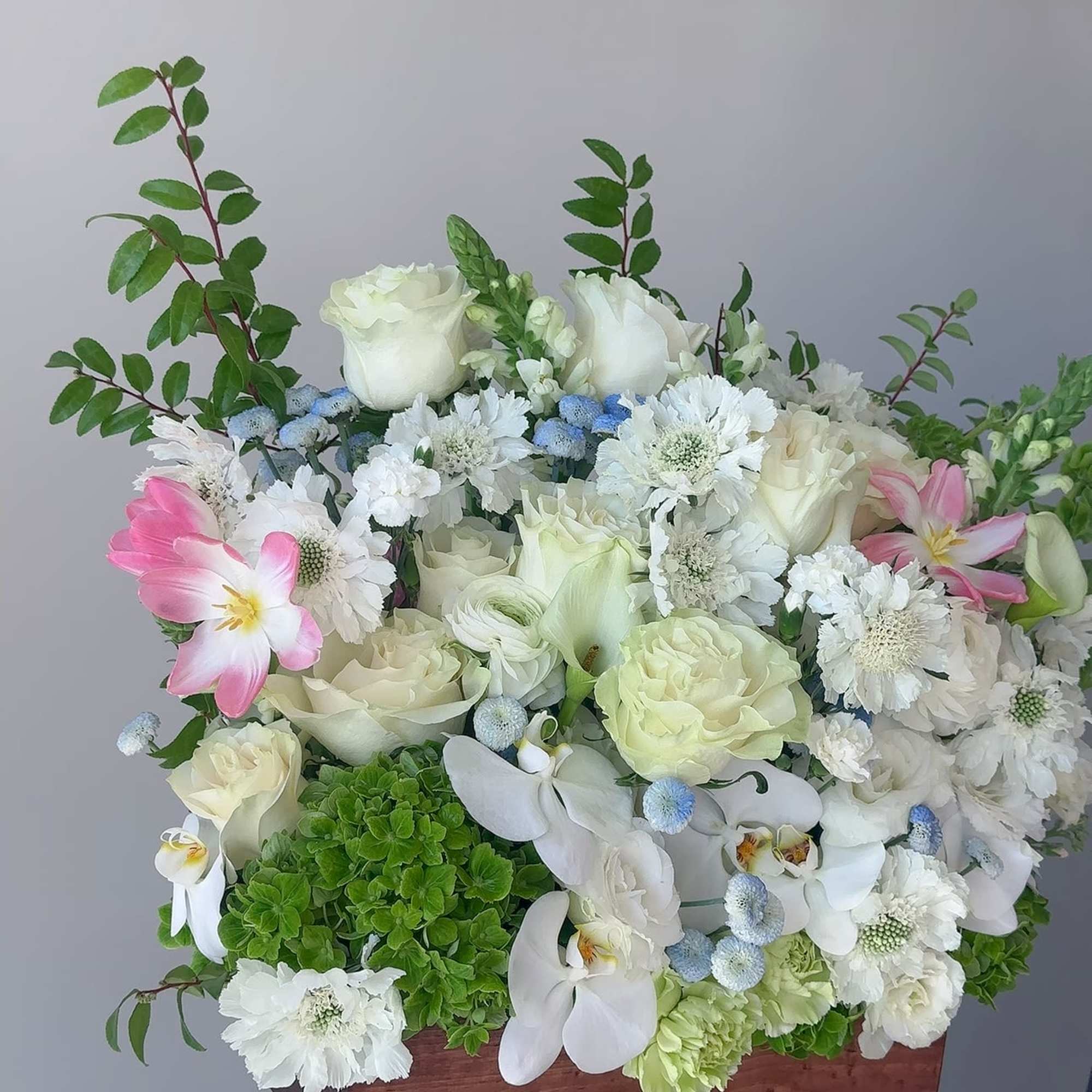 White floral arrangement in a wooden box with pink tulips and orchids