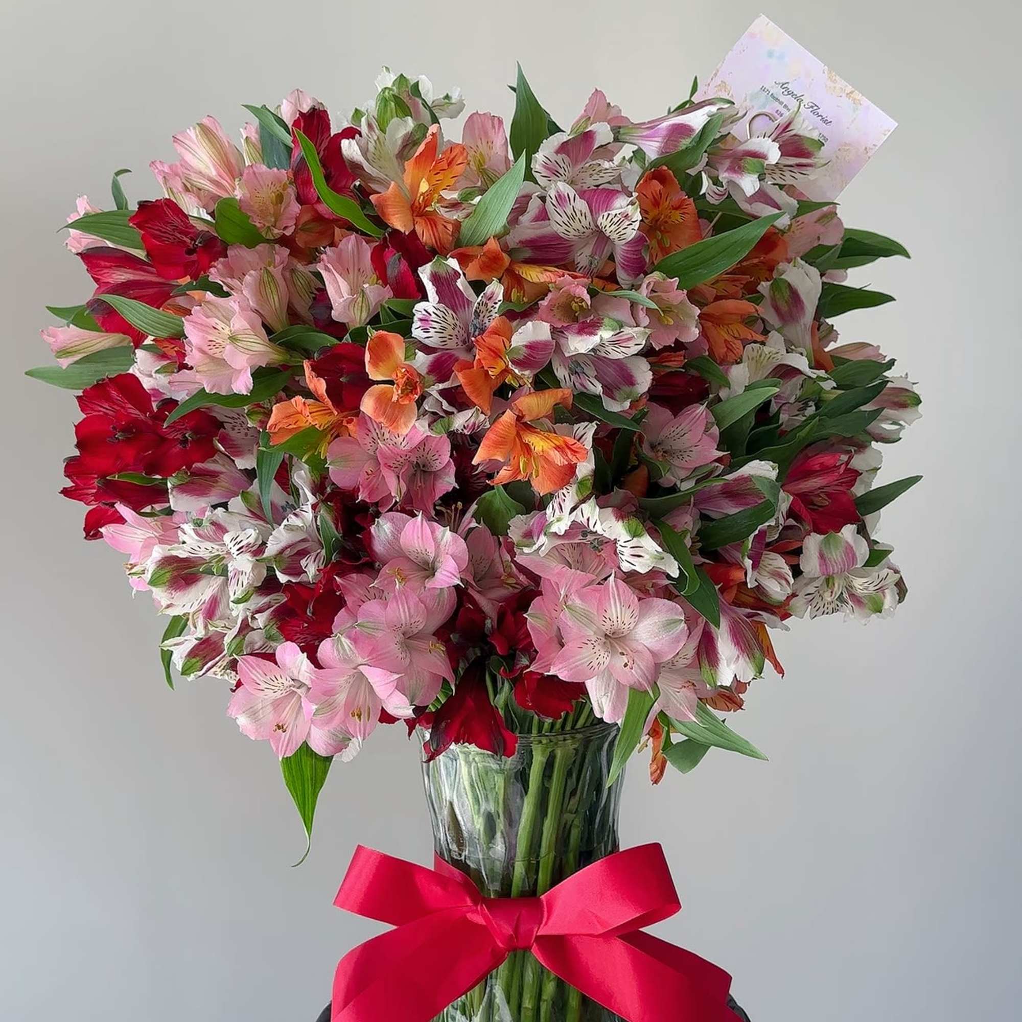 Large bouquet of pink, red, and orange alstroemeria in a glass vase with a red ribbon
