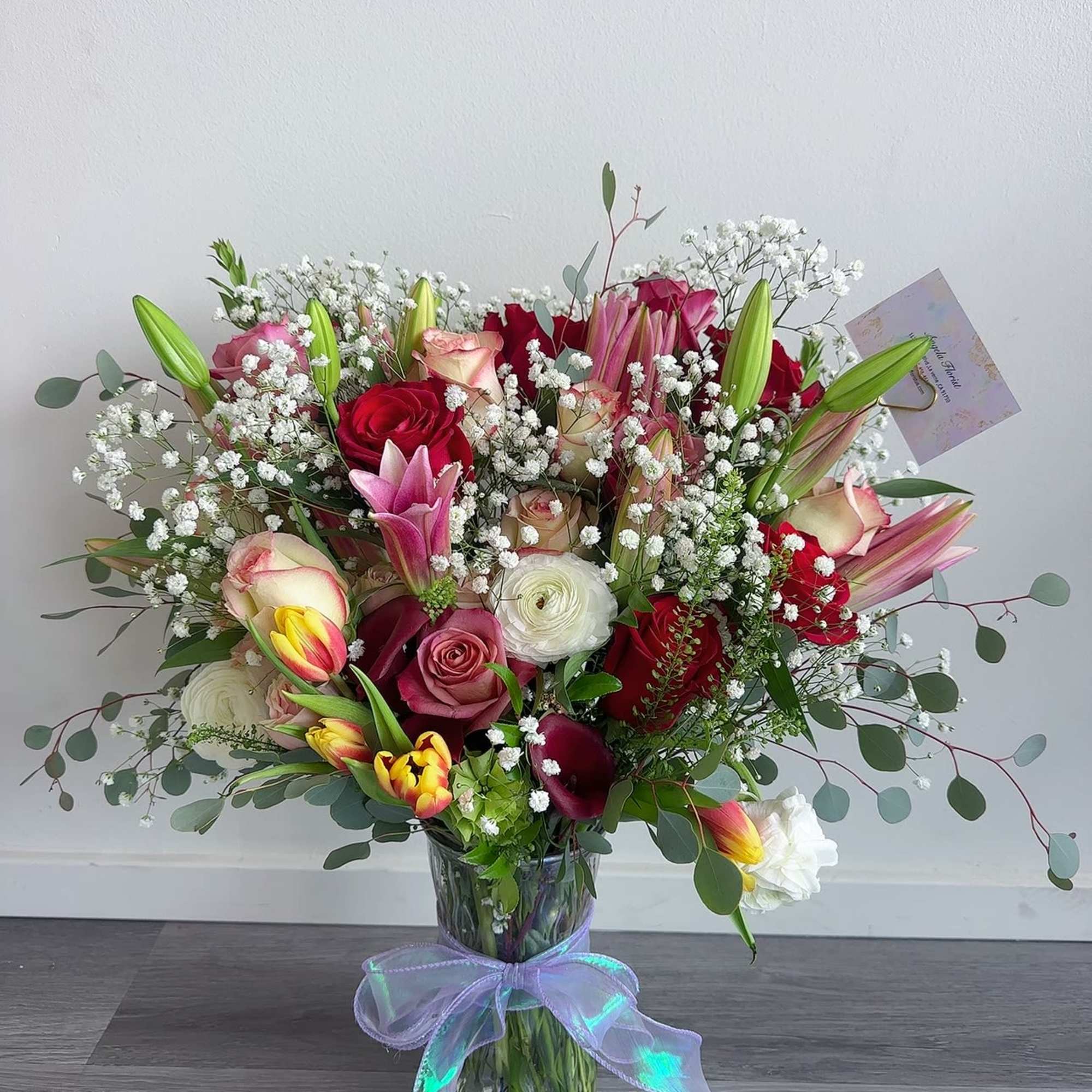 Mixed bouquet of roses, lilies, tulips, and baby's breath in a glass vase