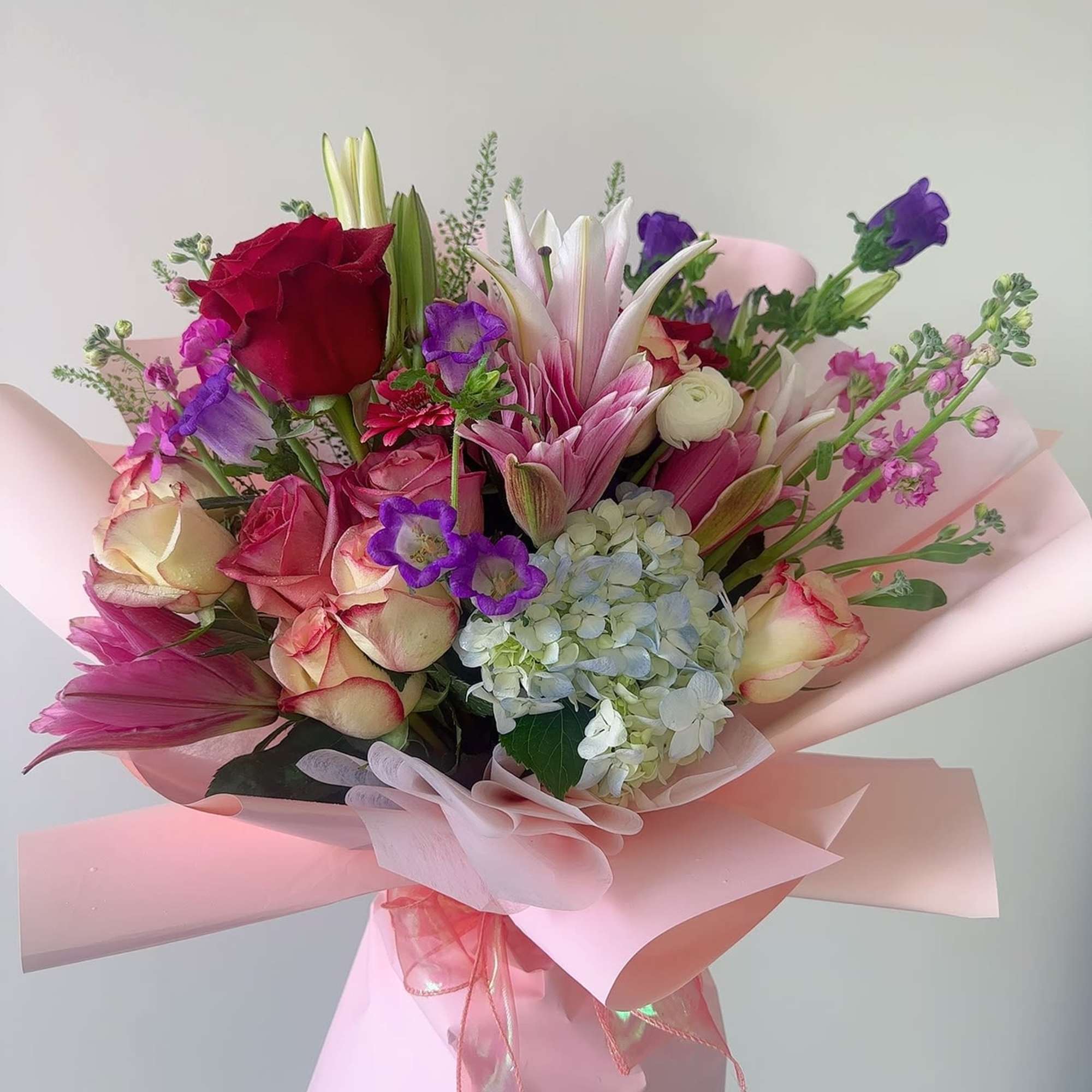 Pink and purple bouquet with roses, lilies, and hydrangea wrapped in pink paper