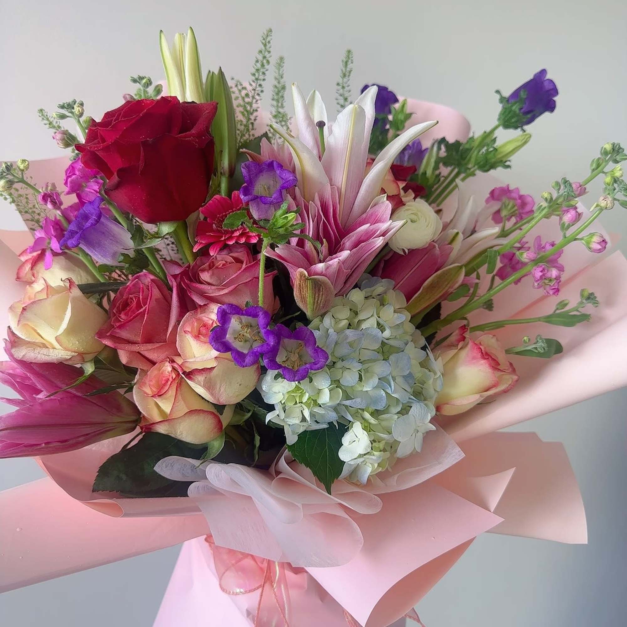 Bouquet of pink and red roses with lilies and hydrangea in pink wrap