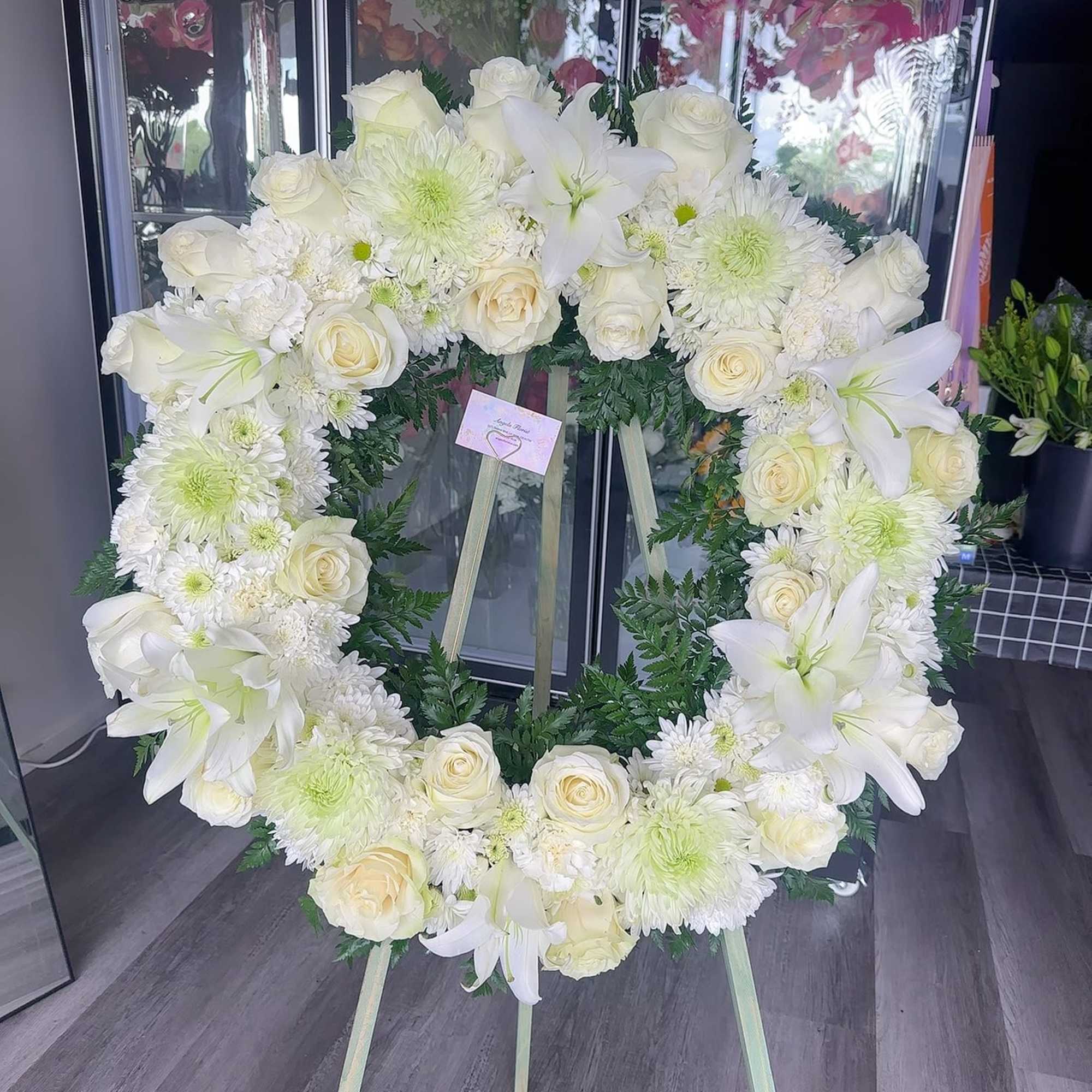 White floral wreath on an easel with roses and lilies