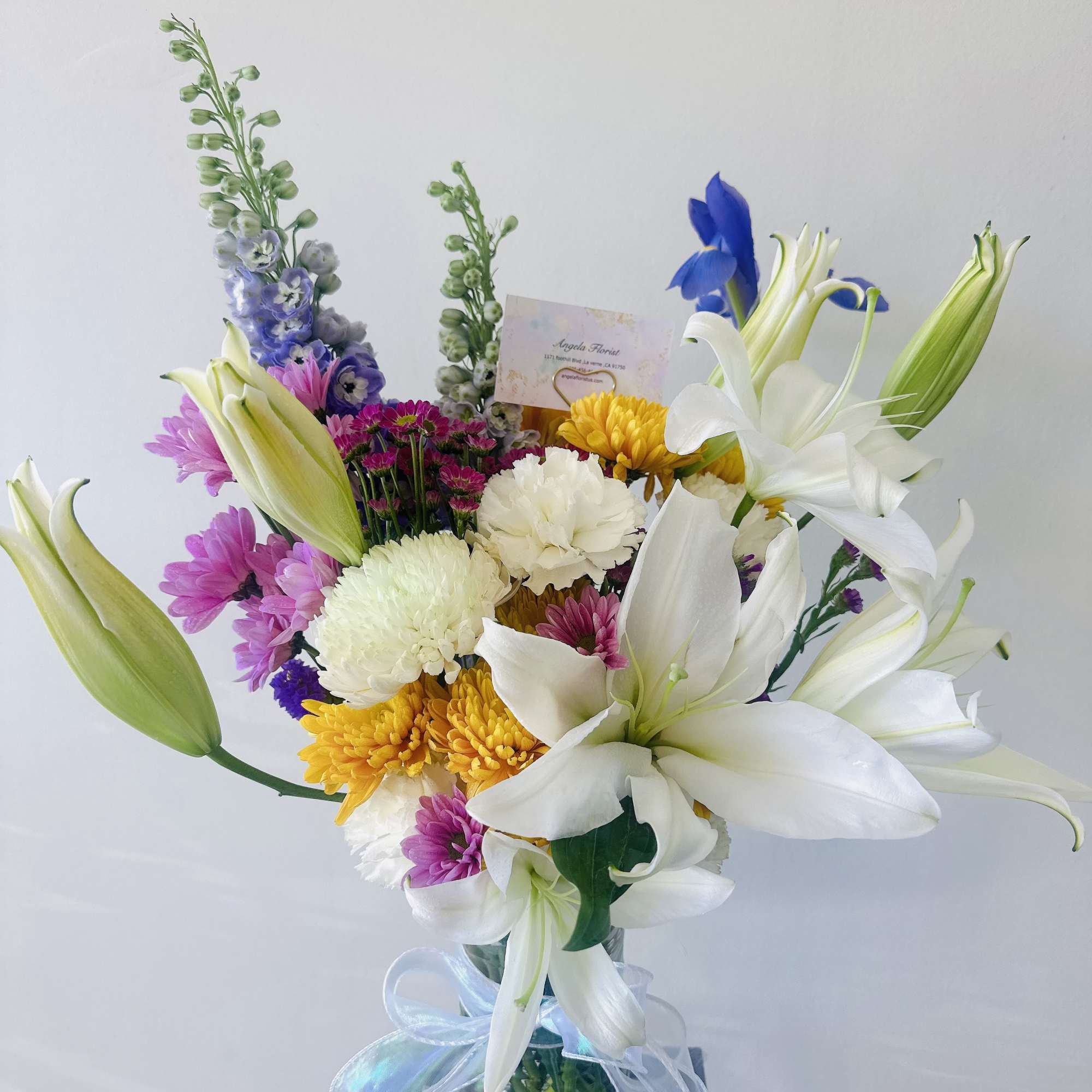 Mixed bouquet with white lilies, chrysanthemums, and purple flowers in a glass vase