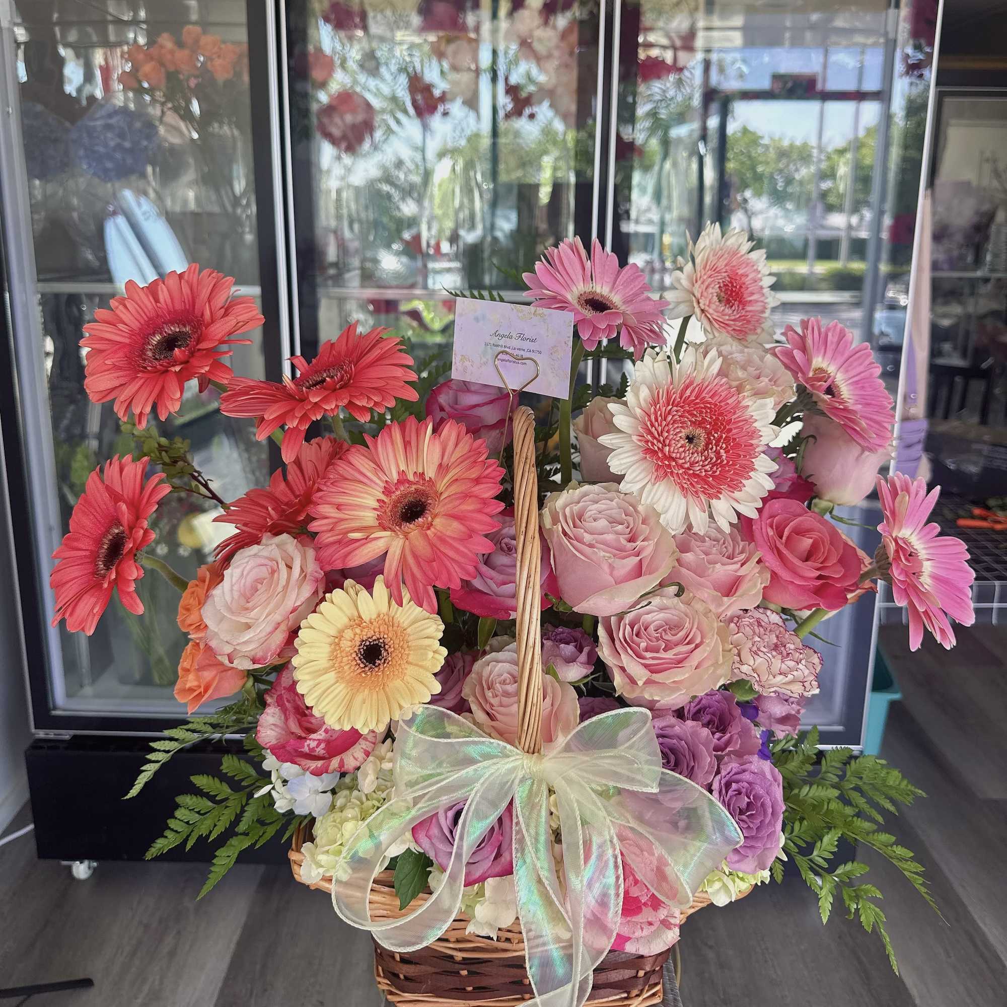 Basket arrangement of pink gerbera daisies and roses with a sheer bow