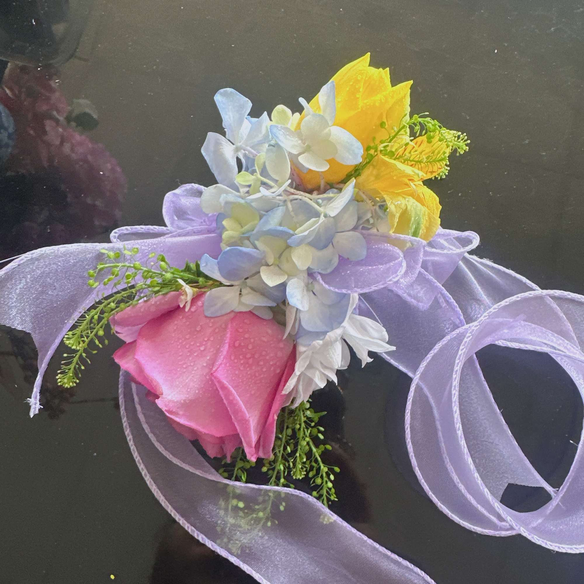 Small bouquet with pink and yellow roses and pale blue flowers tied with lavender ribbon