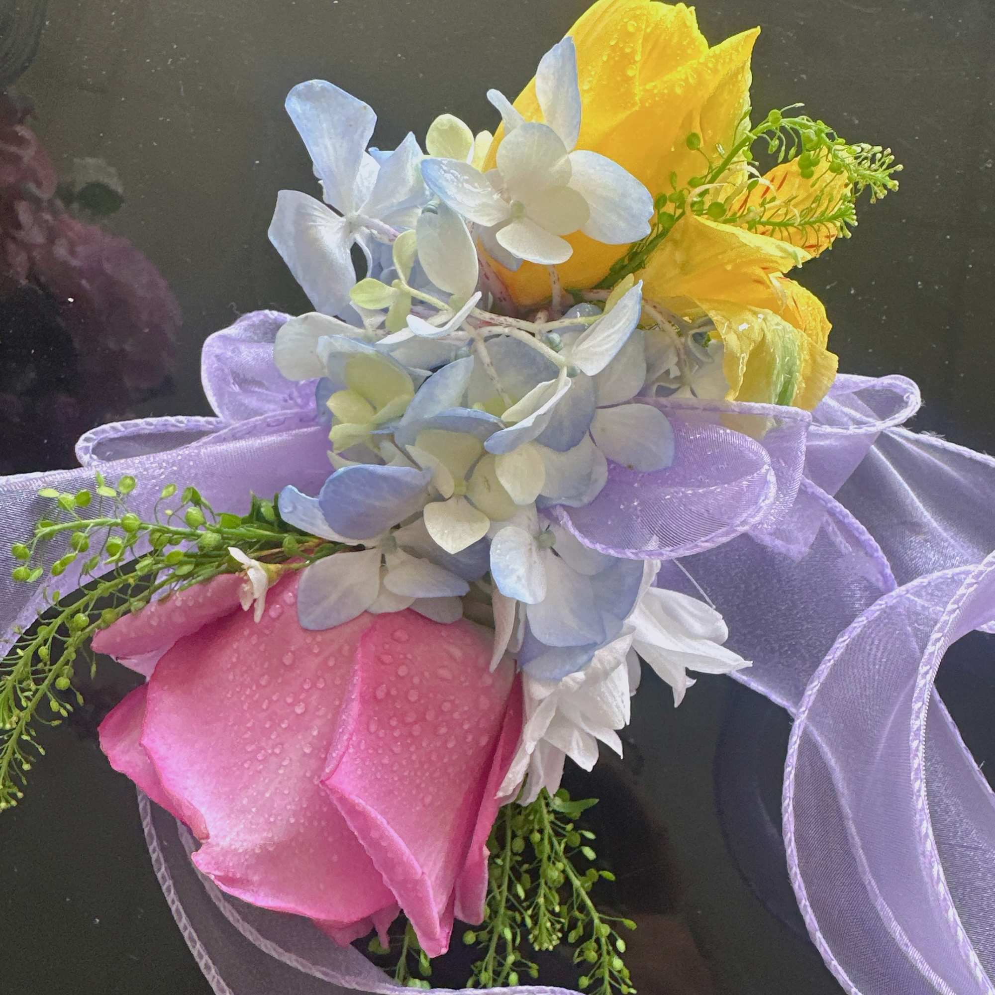 Pink rose boutonniere with blue-white hydrangea and yellow accents on lavender ribbon