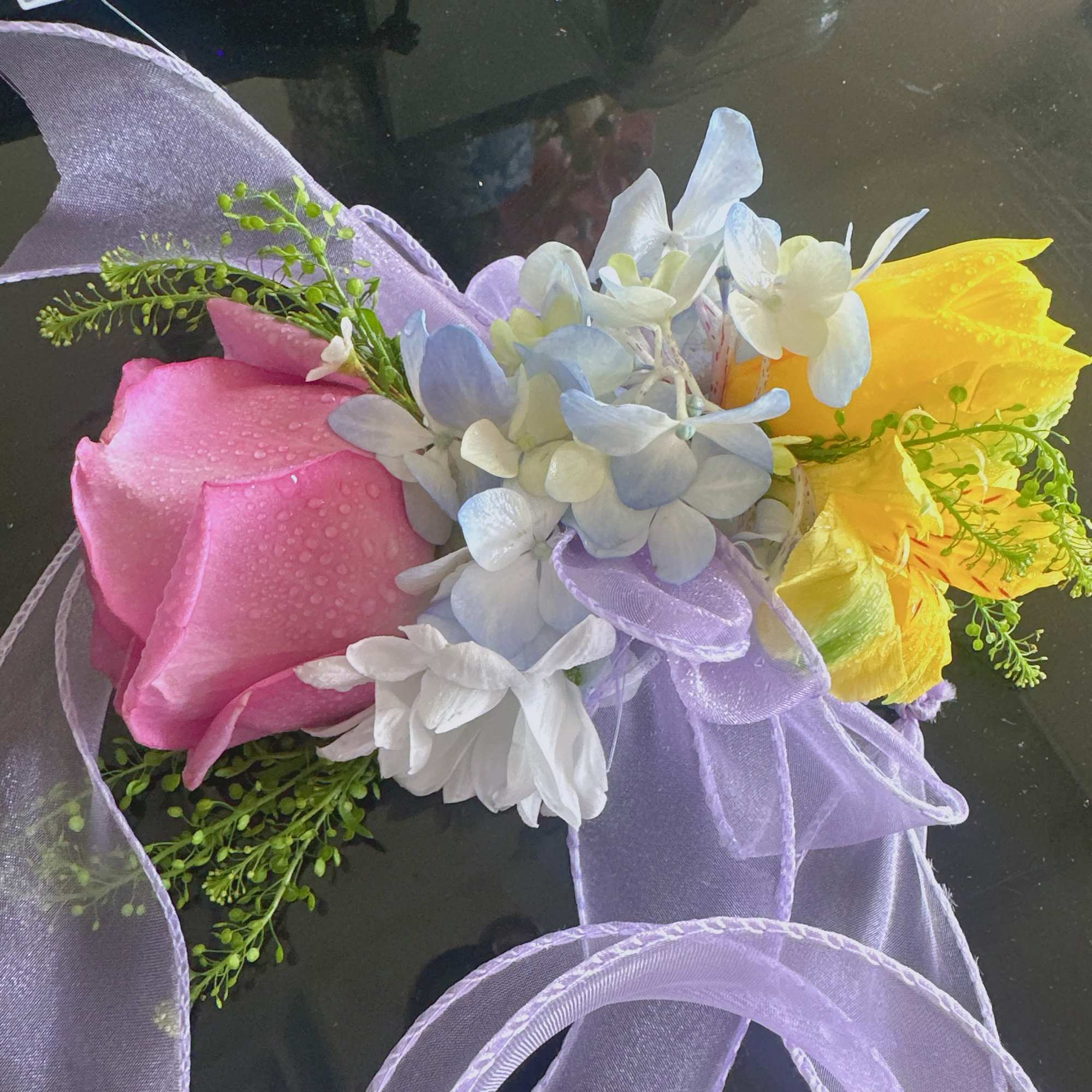 Bouquet of pink, white, blue, and yellow flowers tied with lavender ribbon