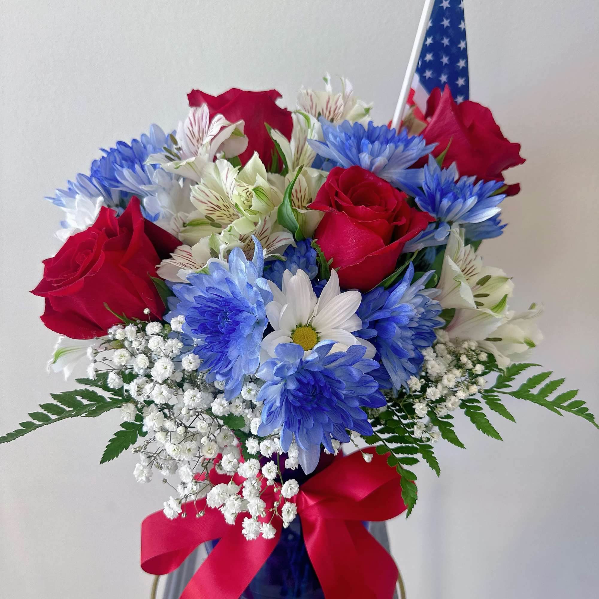 Red roses and blue daisies in a vase with a small American flag