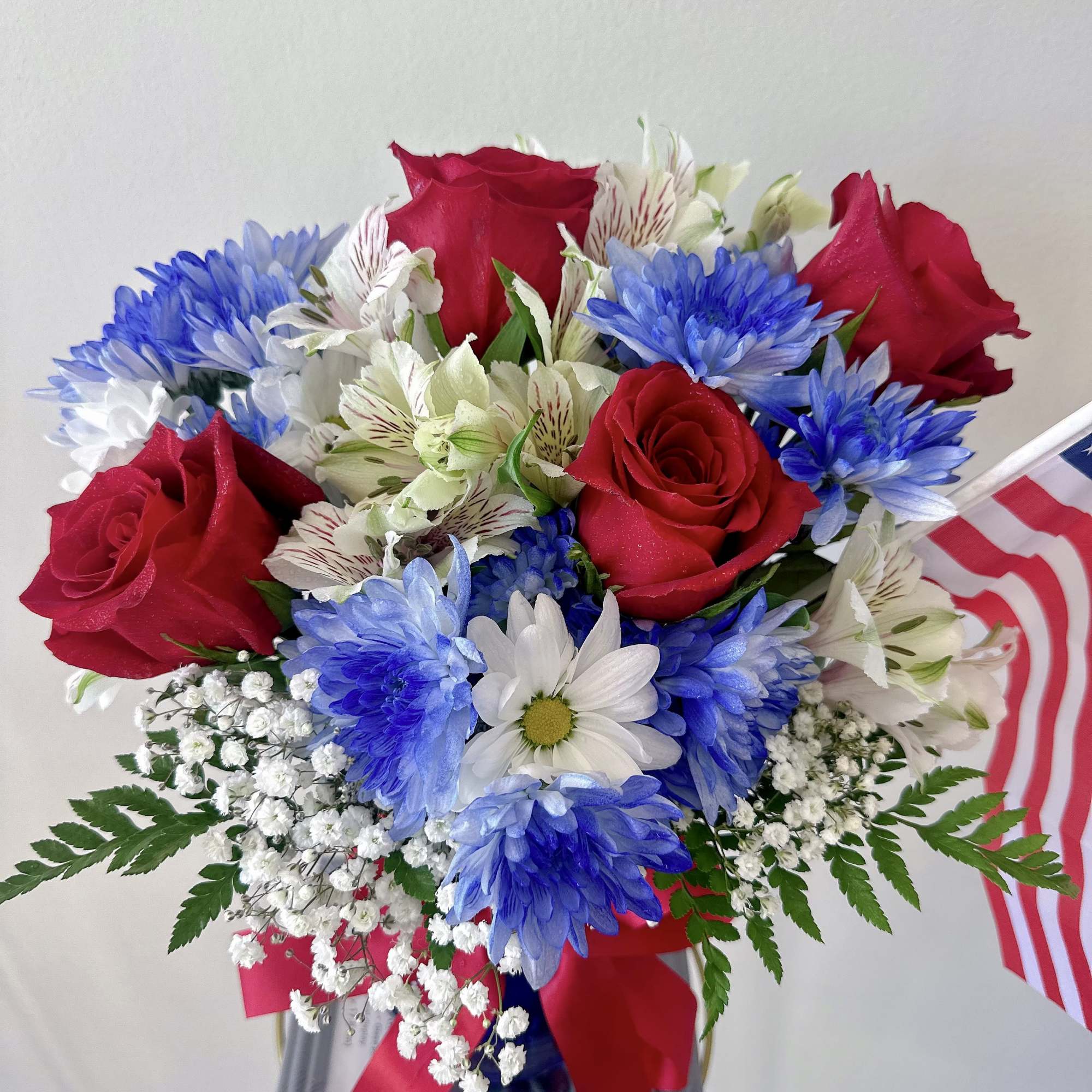 Bouquet of red roses, blue daisies, and white alstroemeria in a vase