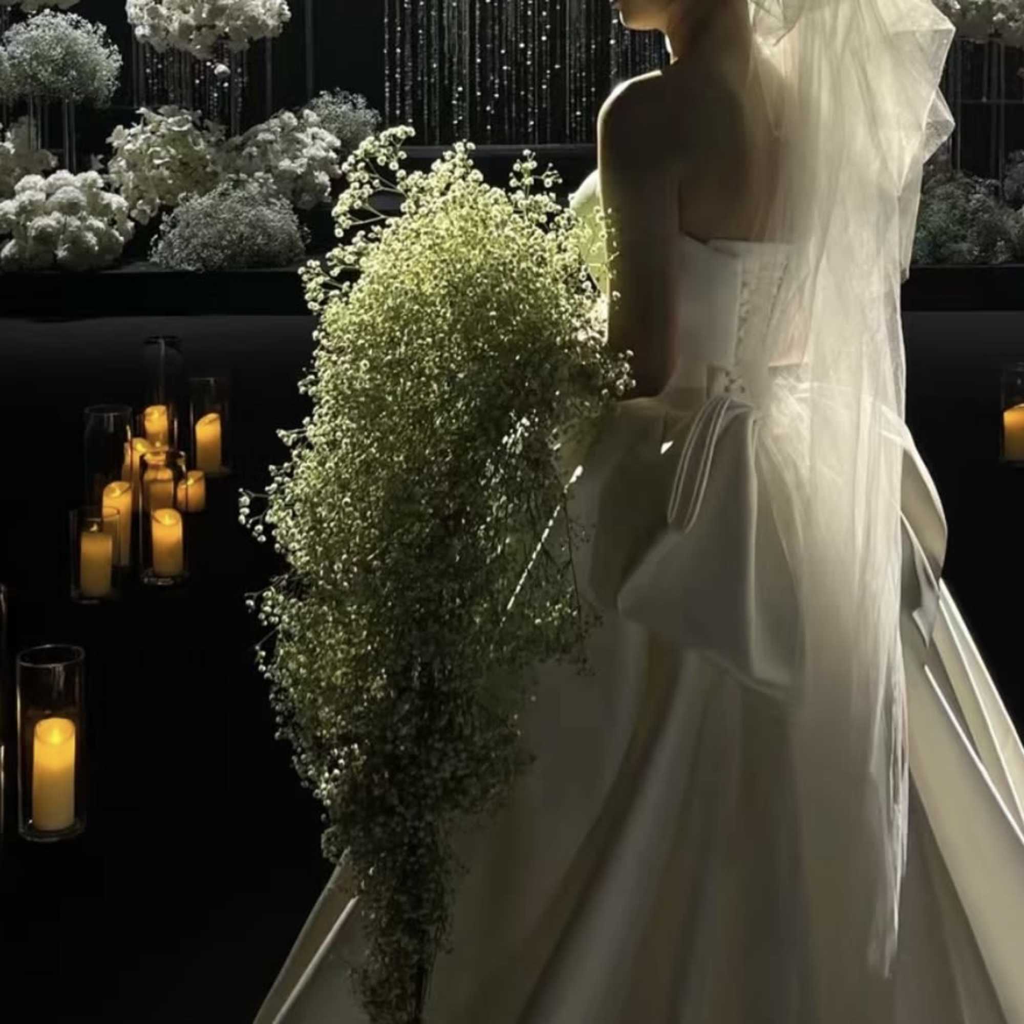 Bride in a white gown holding a cascading bouquet beside candlelit floral decor