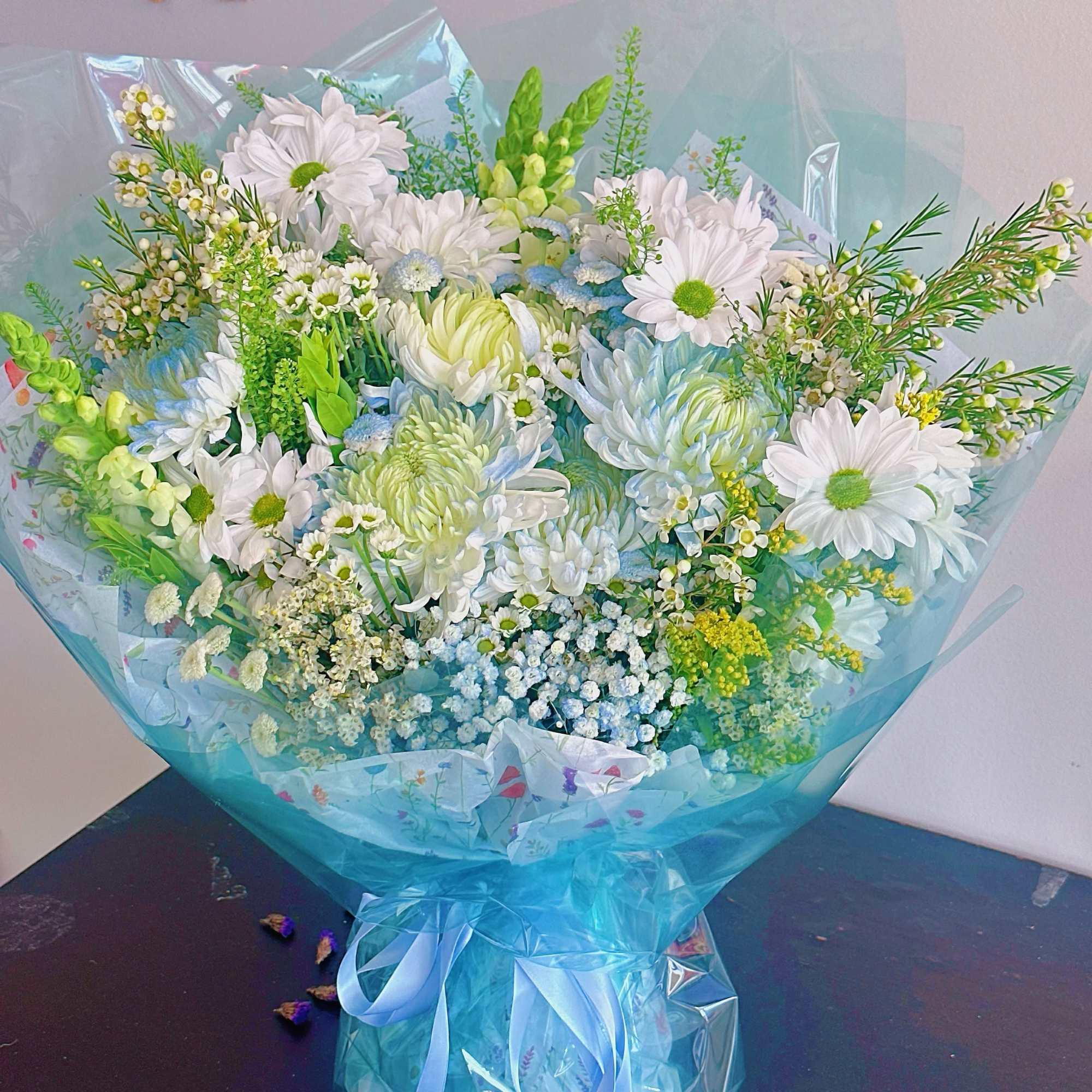 Bouquet of white daisies and pale blue flowers wrapped in blue cellophane