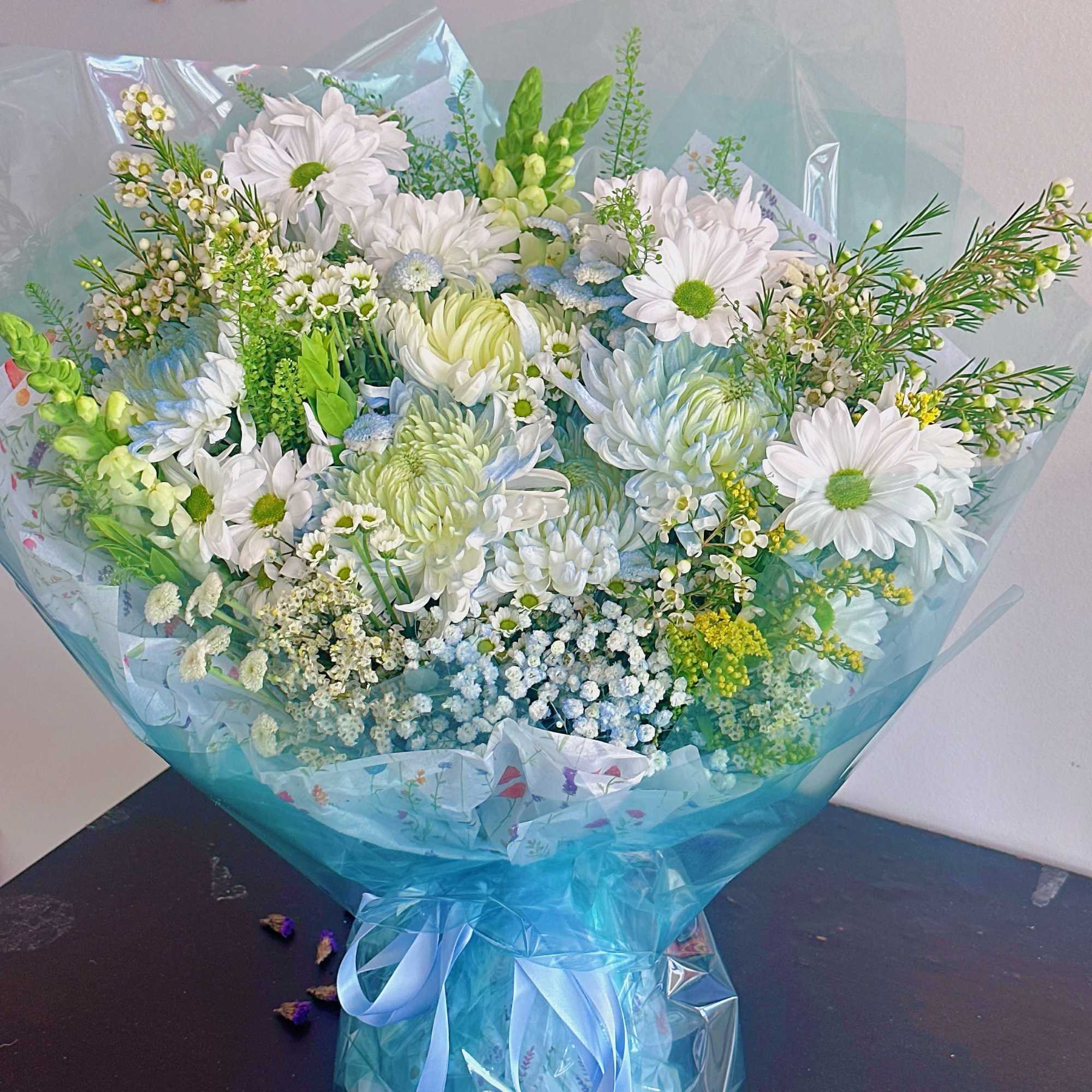 Large bouquet of white and pale blue flowers wrapped in blue cellophane