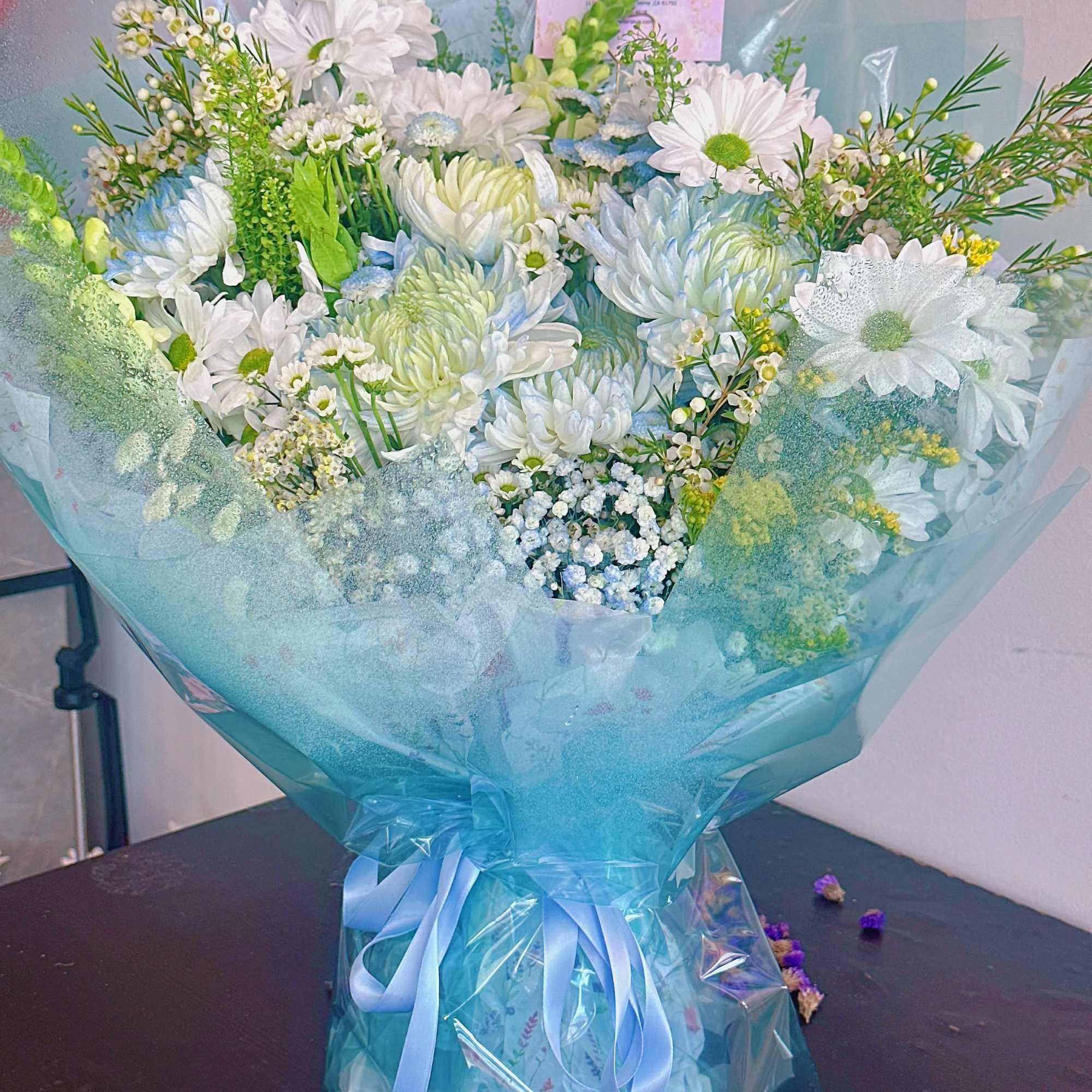 Bouquet of white daisies and blue-tinted flowers wrapped in blue paper