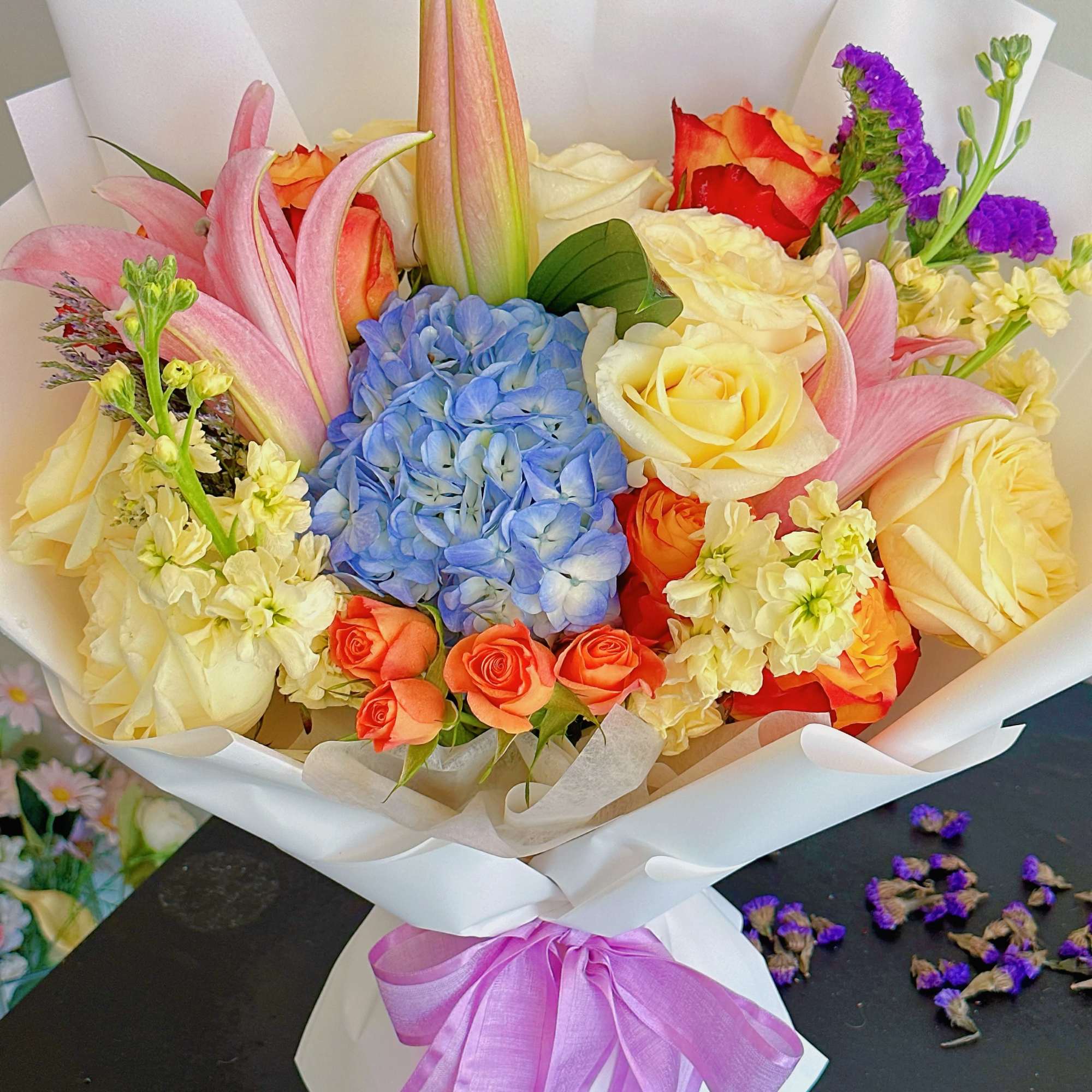 Bouquet of roses, hydrangea, lilies, and purple filler flowers wrapped in white paper
