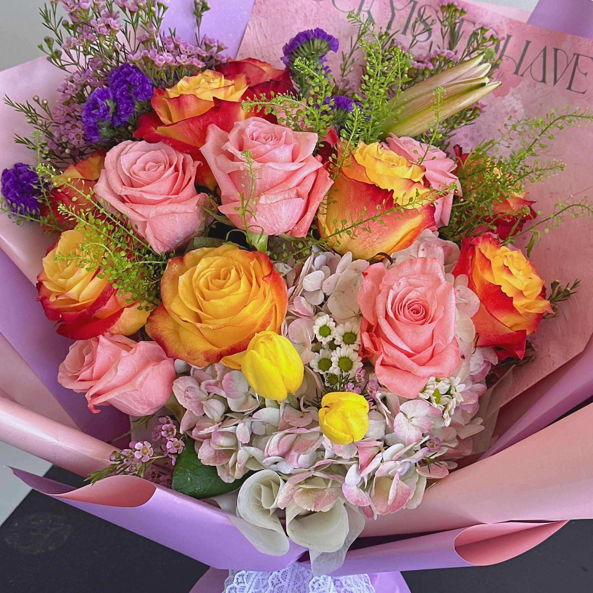 Bouquet of pink and yellow roses with purple accents in pink wrapping