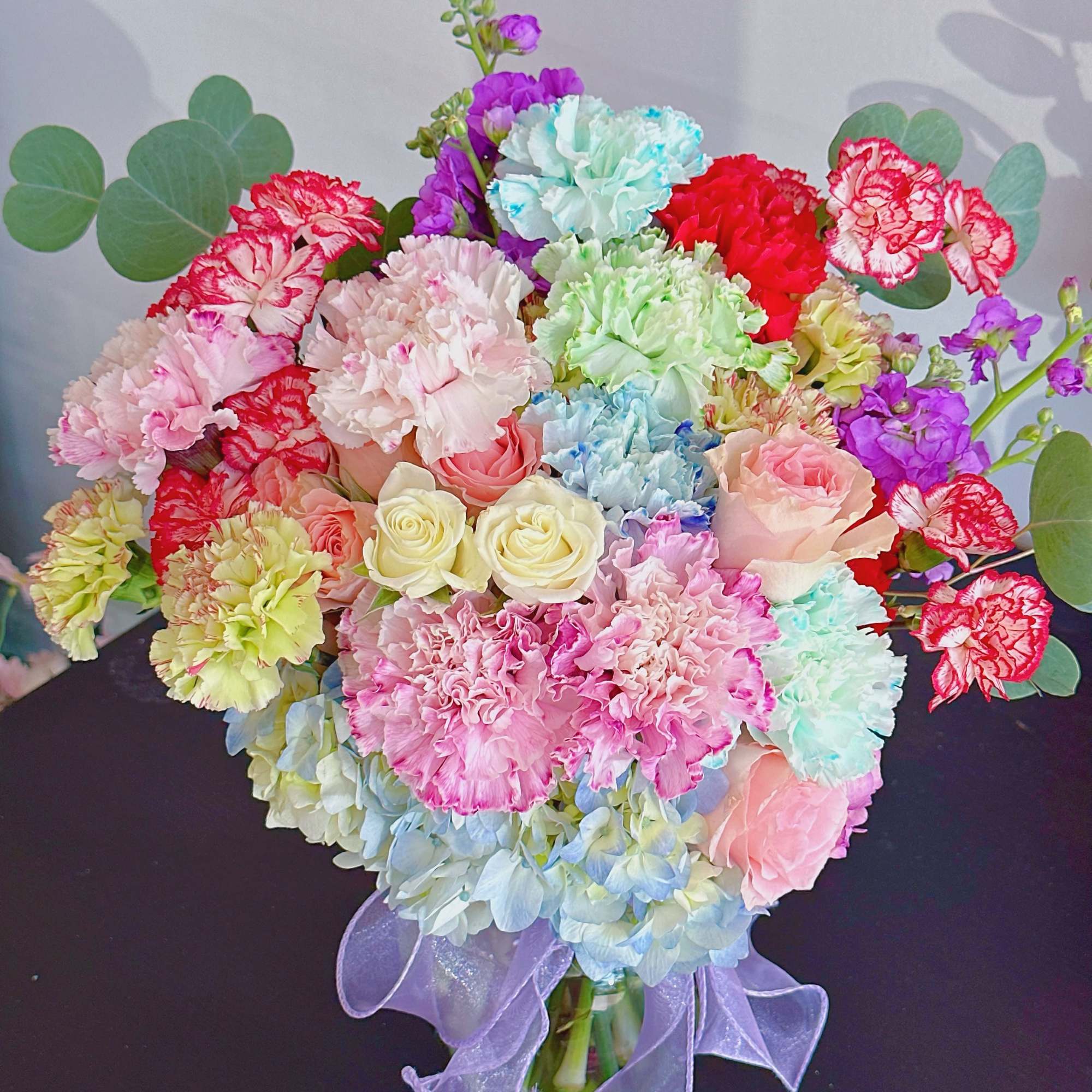 Colorful bouquet of carnations, roses, and hydrangeas in a glass vase with a lavender ribbon, photo 2 of 3