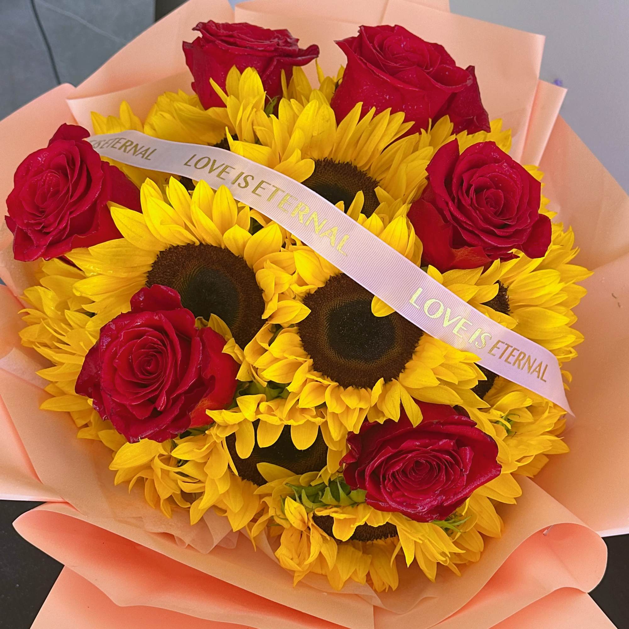 Bouquet of red roses and yellow sunflowers wrapped in peach paper