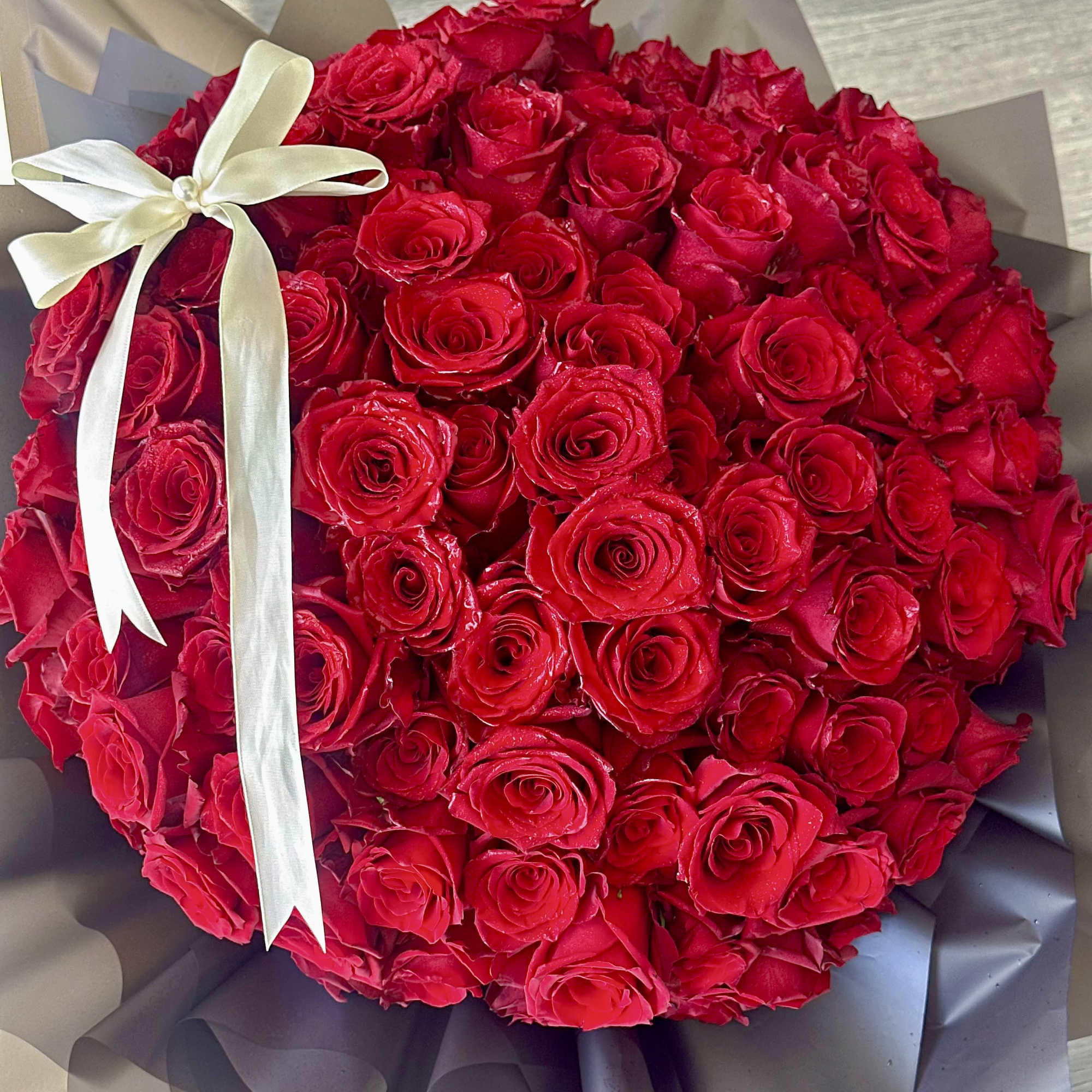Large bouquet of red roses wrapped in dark paper with a white ribbon