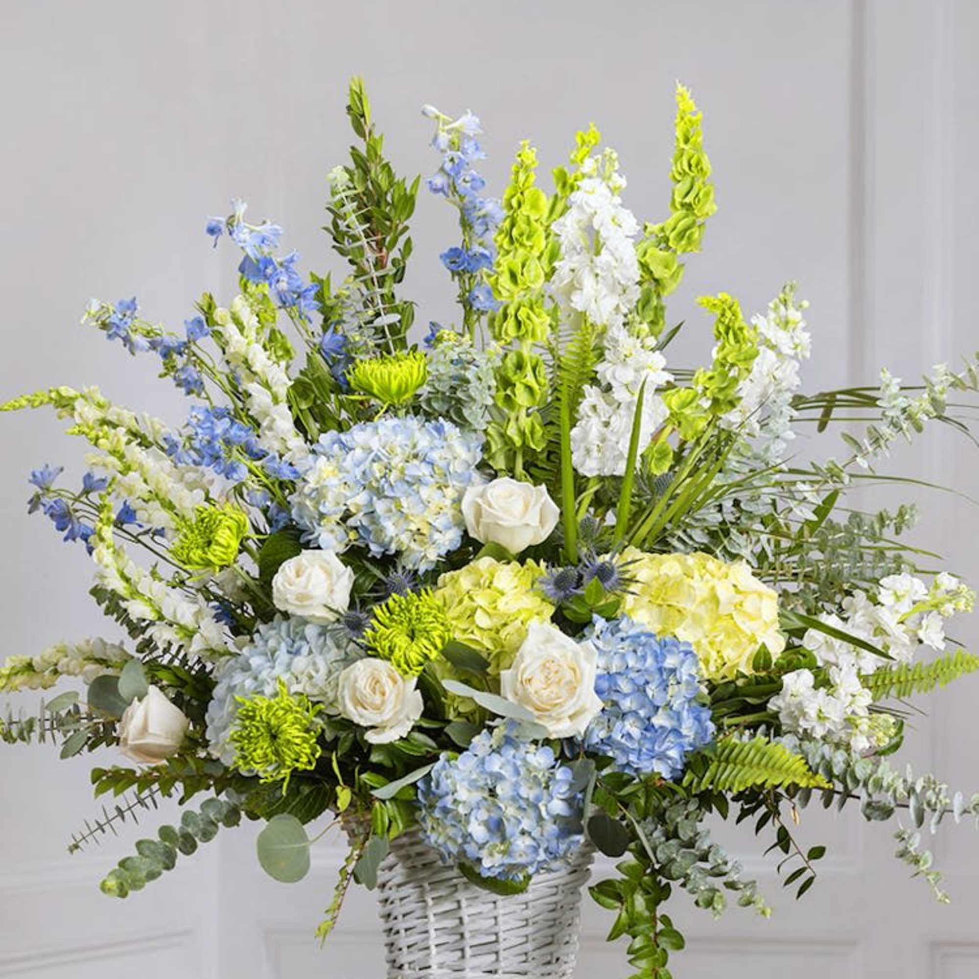 Large floral arrangement in a white wicker basket with blue, white, and green blooms
