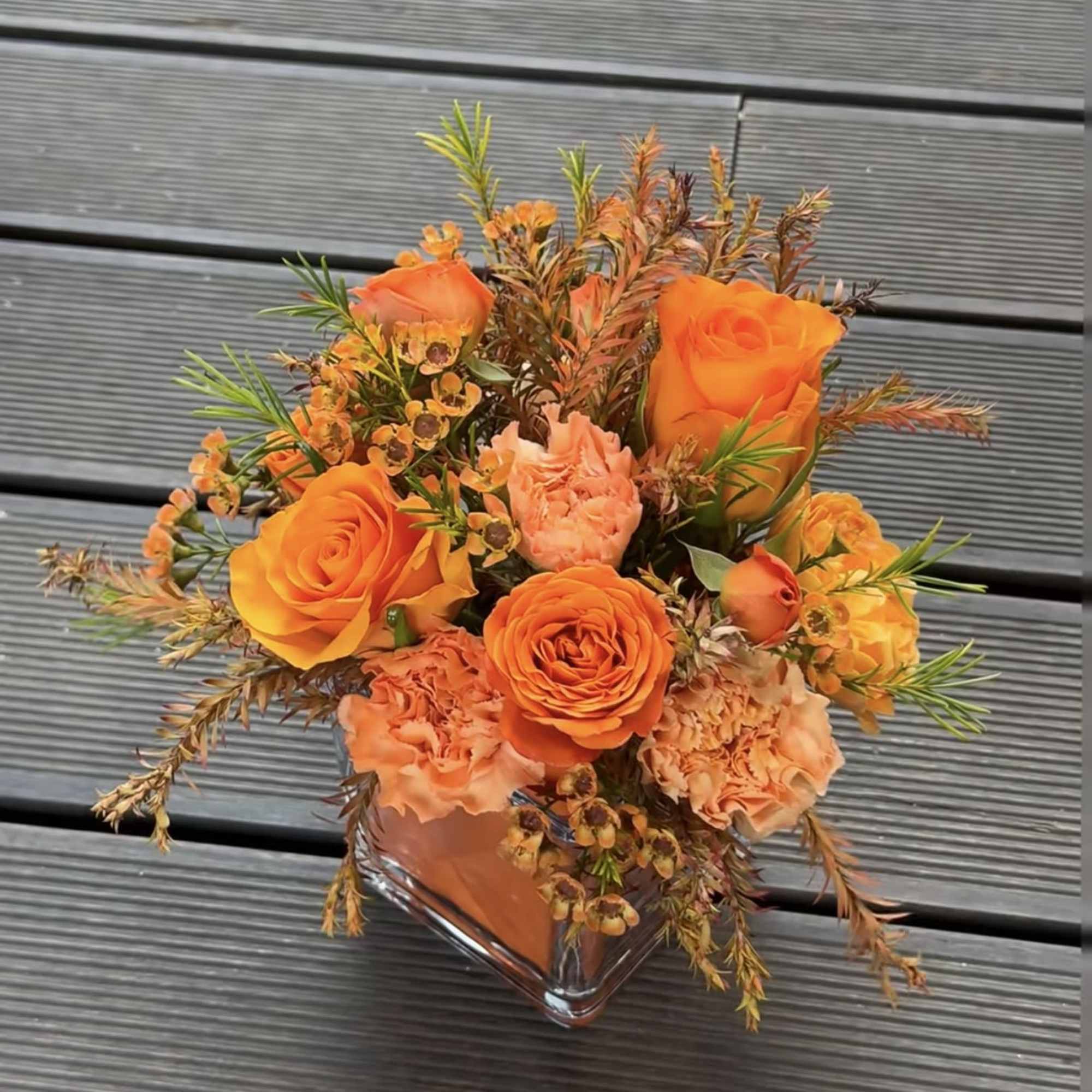 Orange roses and peach carnations in a clear square vase