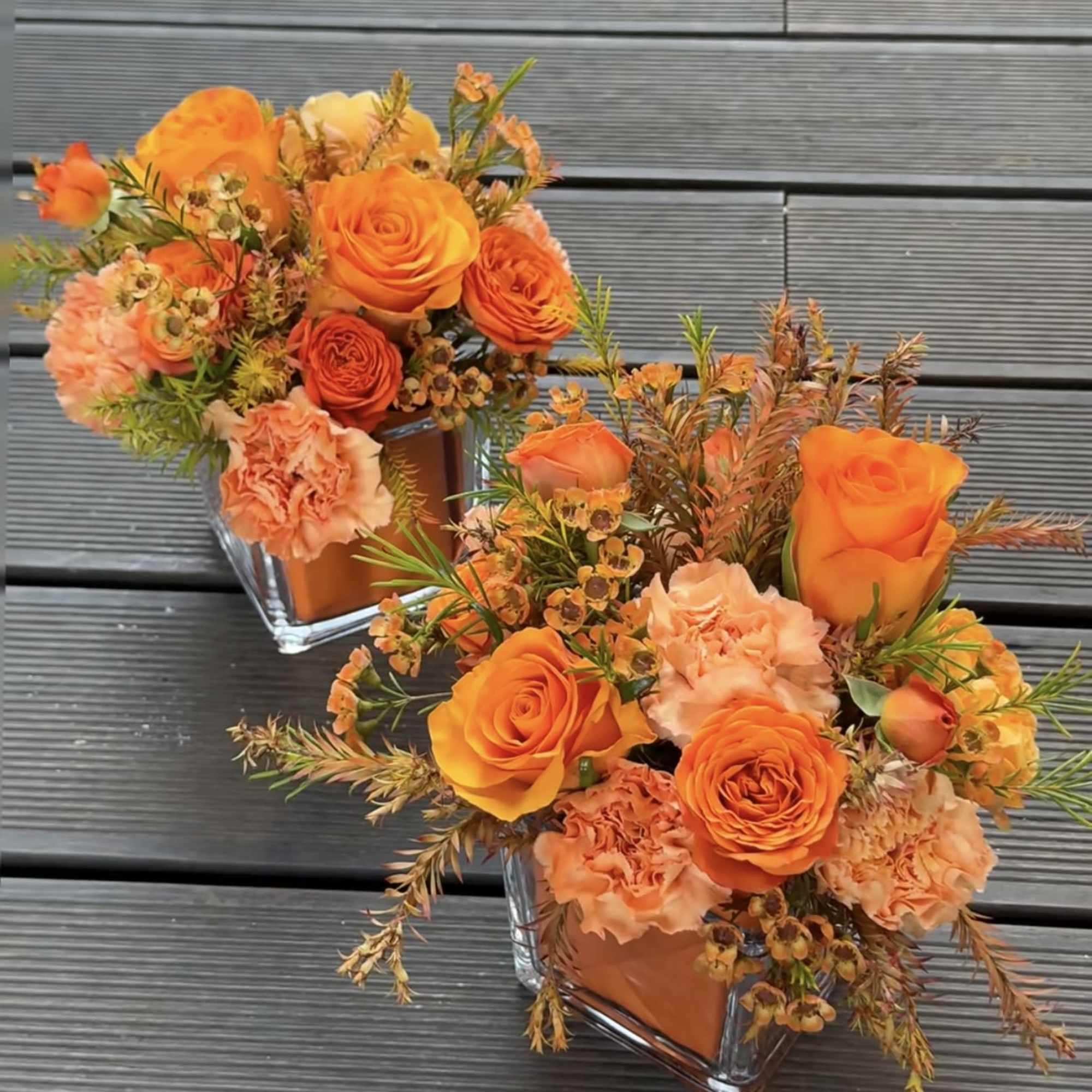 Two orange floral arrangements in square glass vases